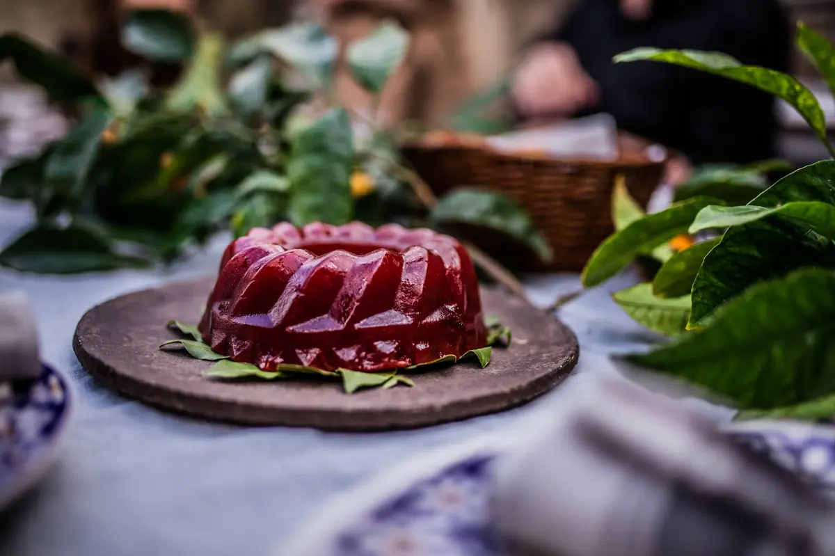 A red round jelly-like dessert served on a bed of bay leaves on a tray.