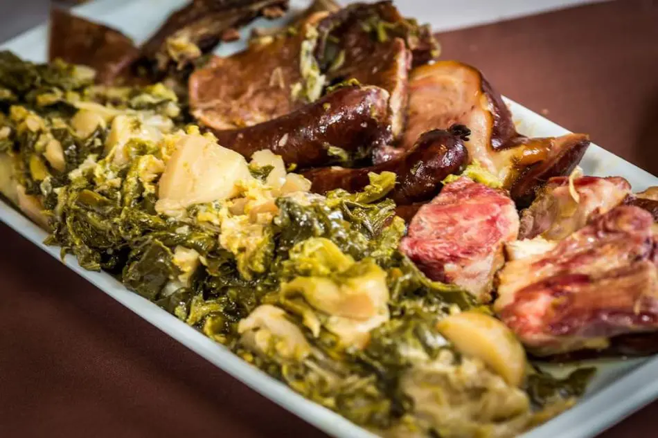 A white plate with boiled greens, pieces of meat, and sausage.