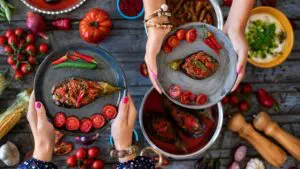 This is a close-up of the hands of two women holding one dish of imam bayildi (stuffed eggplant) each.
