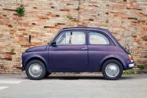 This image shows a vintage Fiat 500 parked in front of a brick wall. Fiat 500 tours in Italy are among the best classic car tours in Europe.