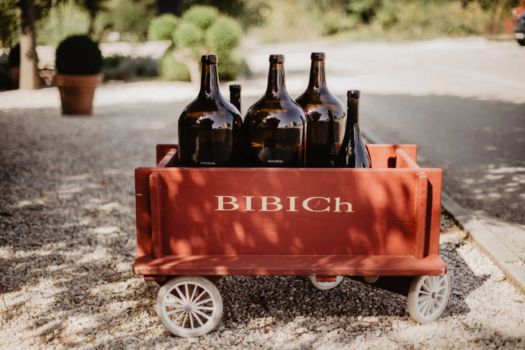 This image shows five brown glass bottles of varying sizes inside a small wooden cart that reads Bibich, one of the top wineries in Split.