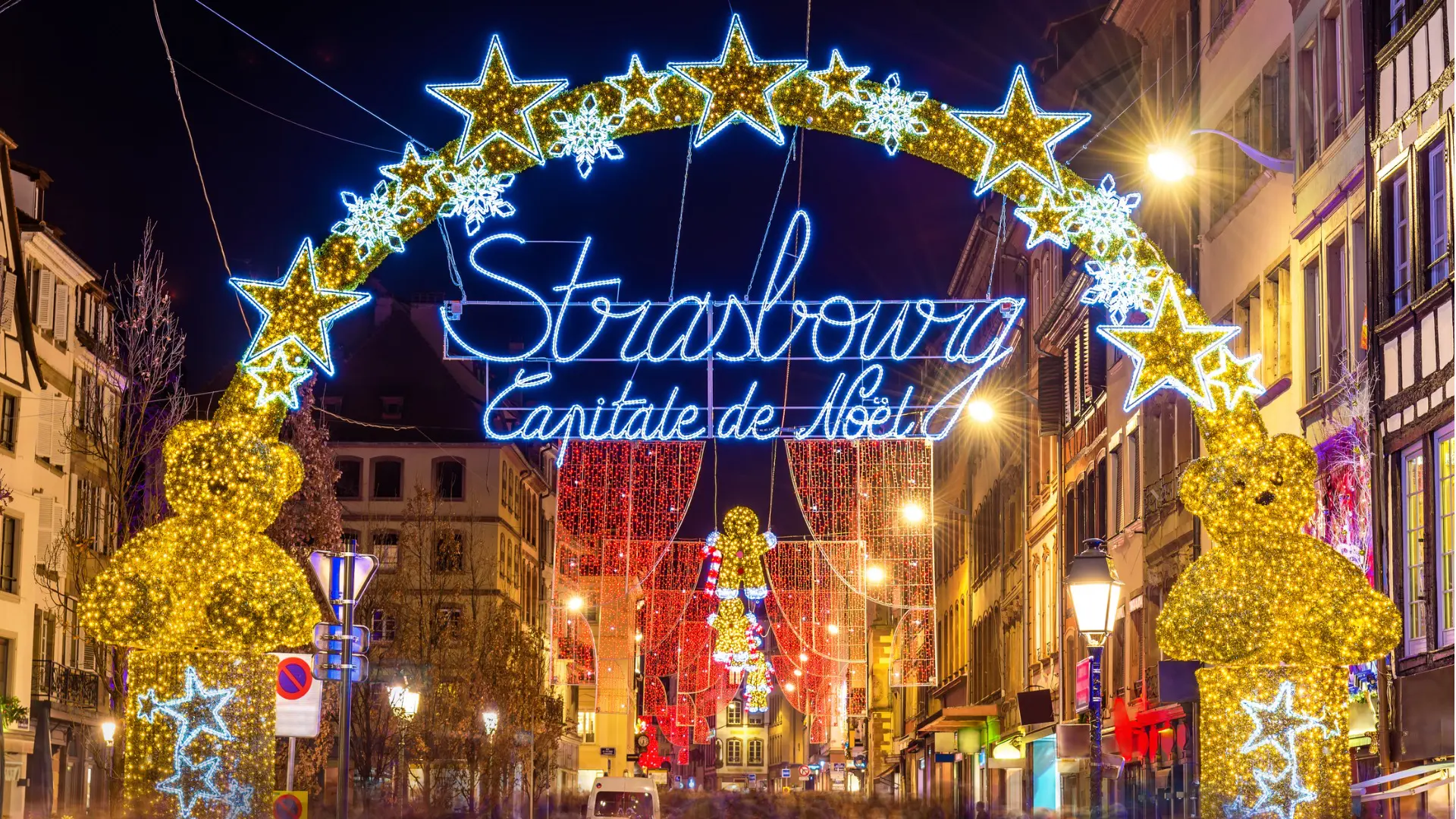 An illuminated sign that reads Strasbourg Capitale de Noel with beautiful buildings and Christmas lights in the background.