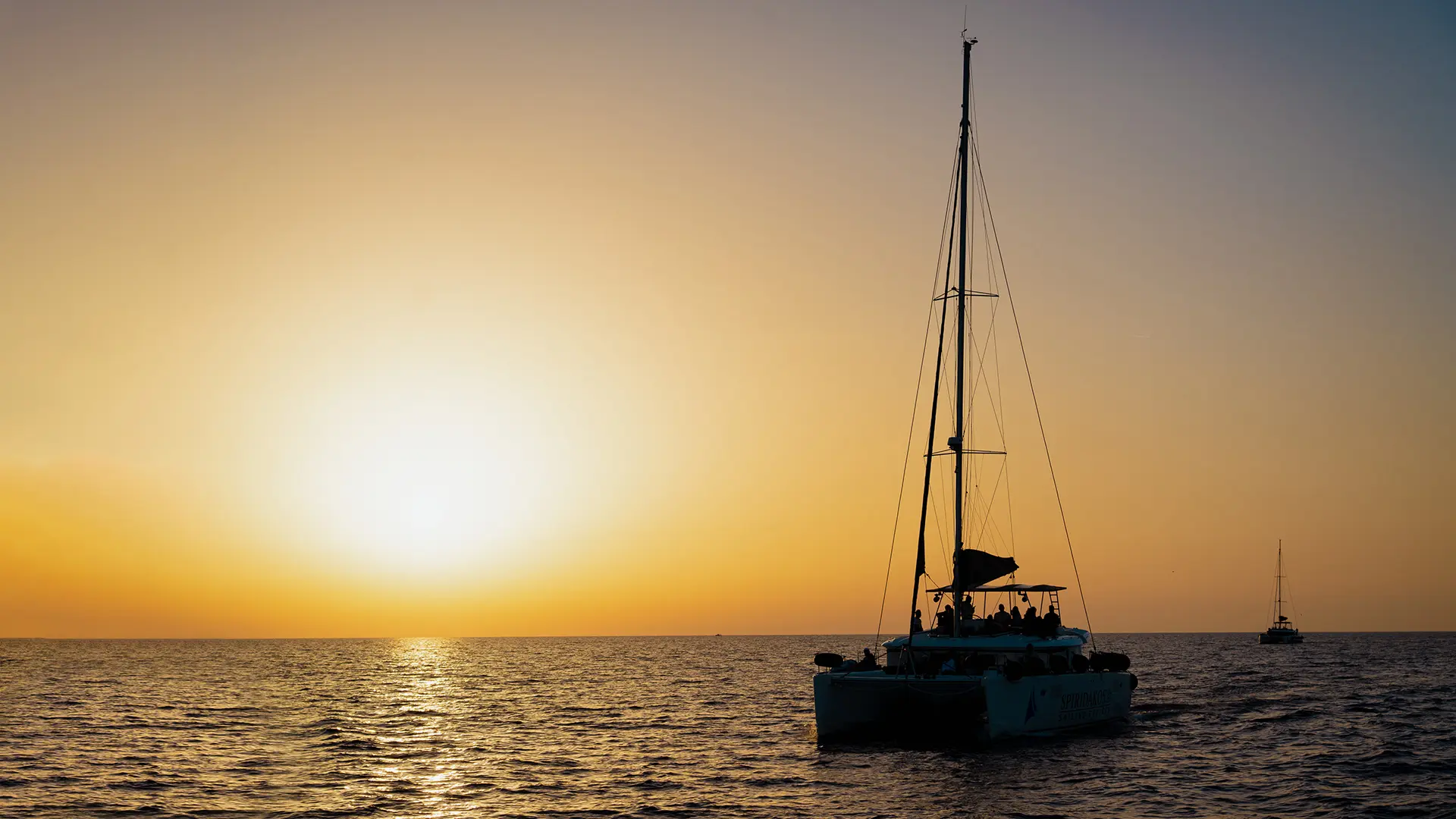 This image shows a sailing catamaran at sunset.