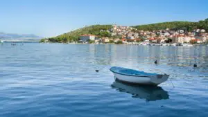 This image shows a small boat in the calm sea, with a red-rooftoped town in the background.