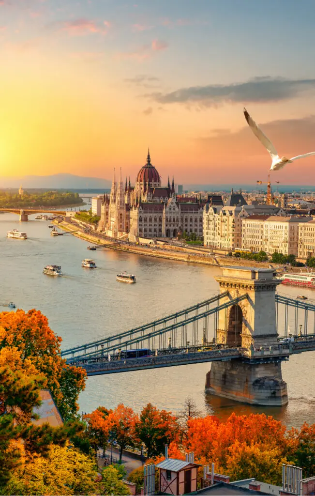 A view of Budapest at sunset with the chain bridge in the foreground, and the iconic Hungarian Parliament building in the background.