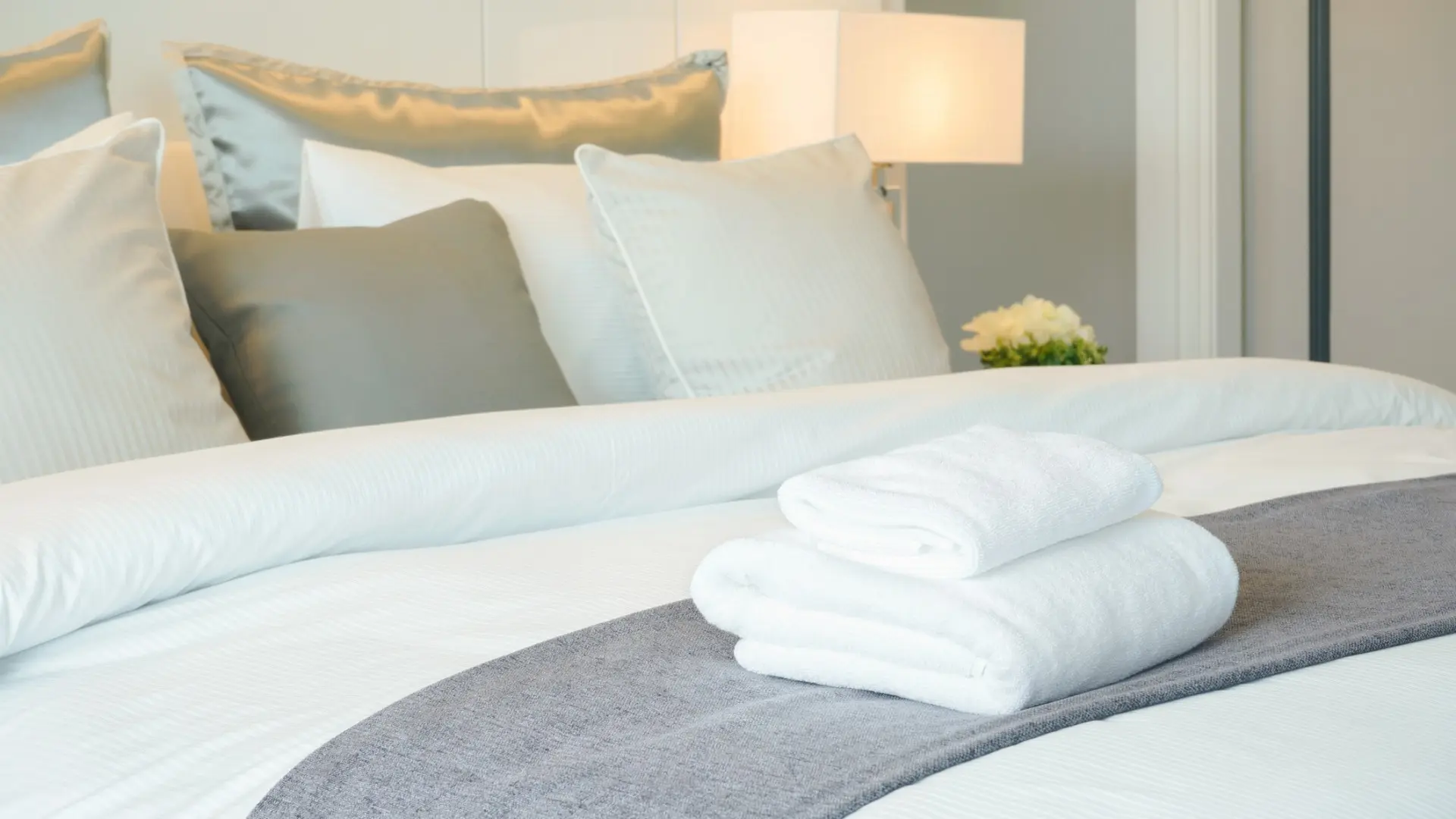 This is a close-up of a hotel bedroom. The bed is set and there are two fresh towels on the bed.