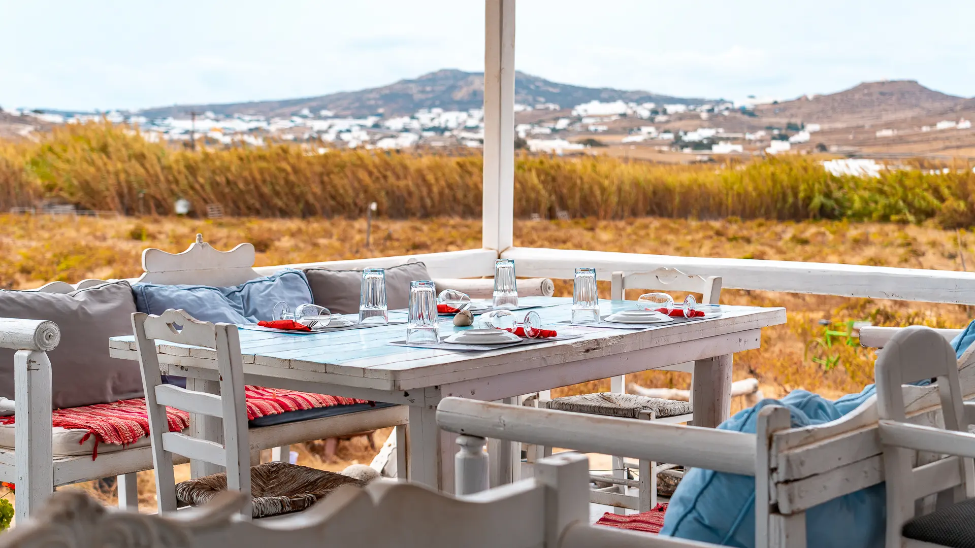 This image shows a table set for lunch with the natural landscape of Mykonos in the background.