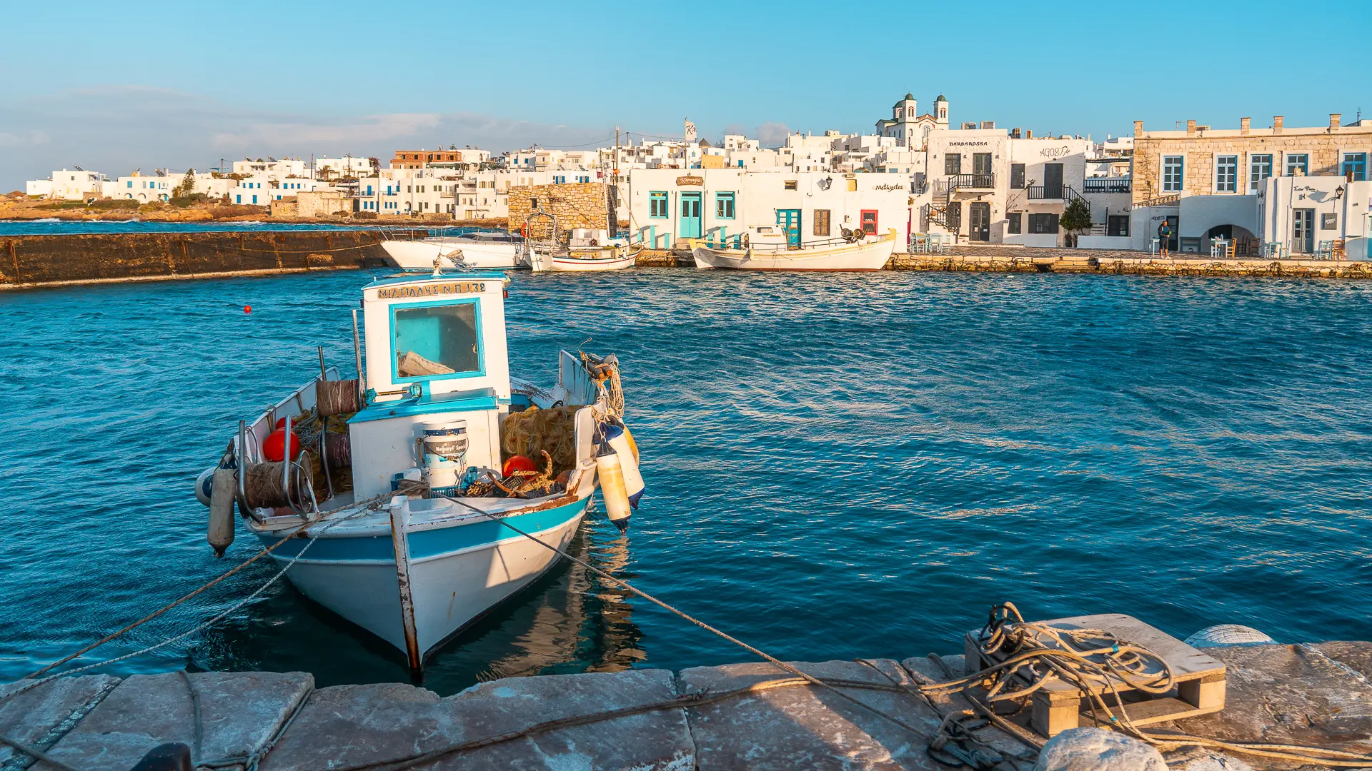 This image shows the quaint Old Port of Naoussa in the background and a wooden fishing boat in the foreground.