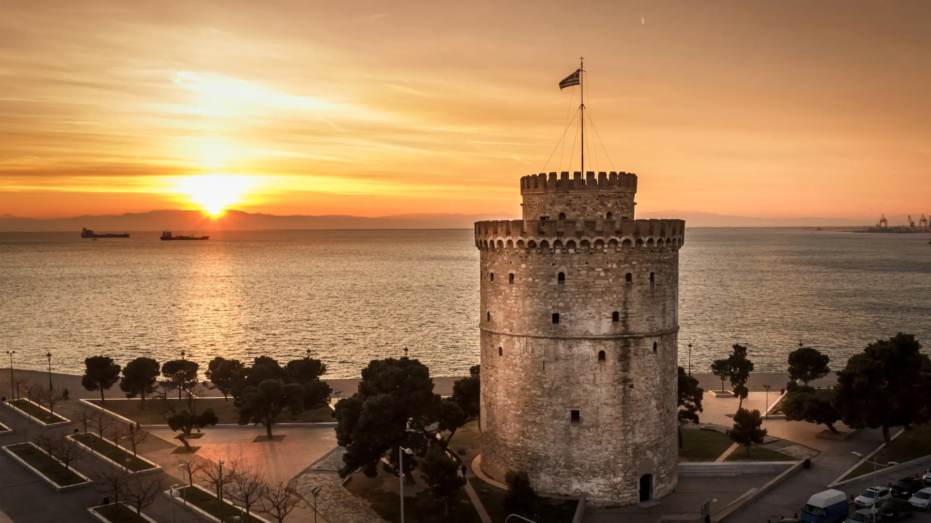 This image shows the White Tower in the foreground and the sun setting behind a mountain in the background.