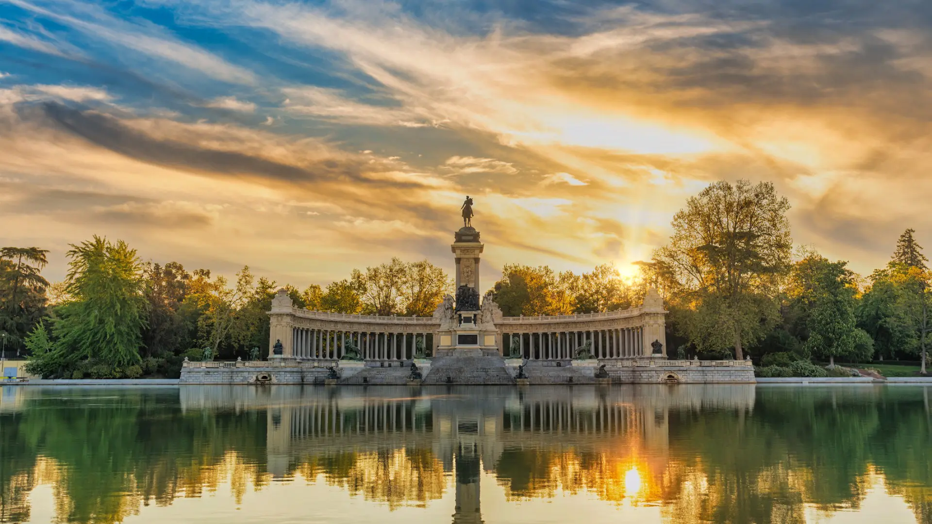 The large artificial lake of El Retiro Park at sunset. In the background, the grandiose Monument to Alfonso XII.