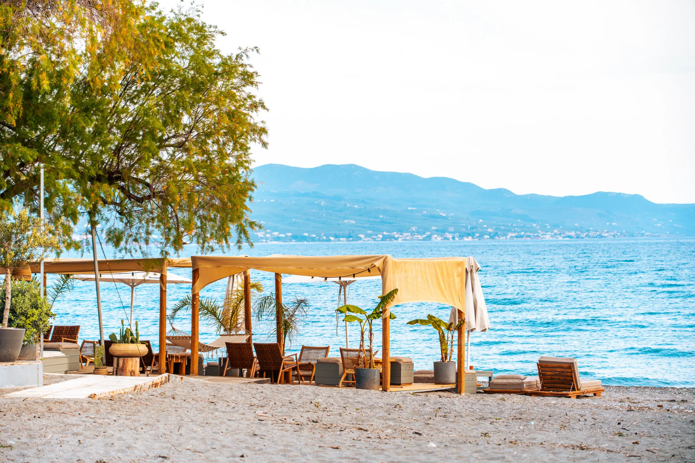 This image shows a beach café right by the calm sea and mountains in the background.