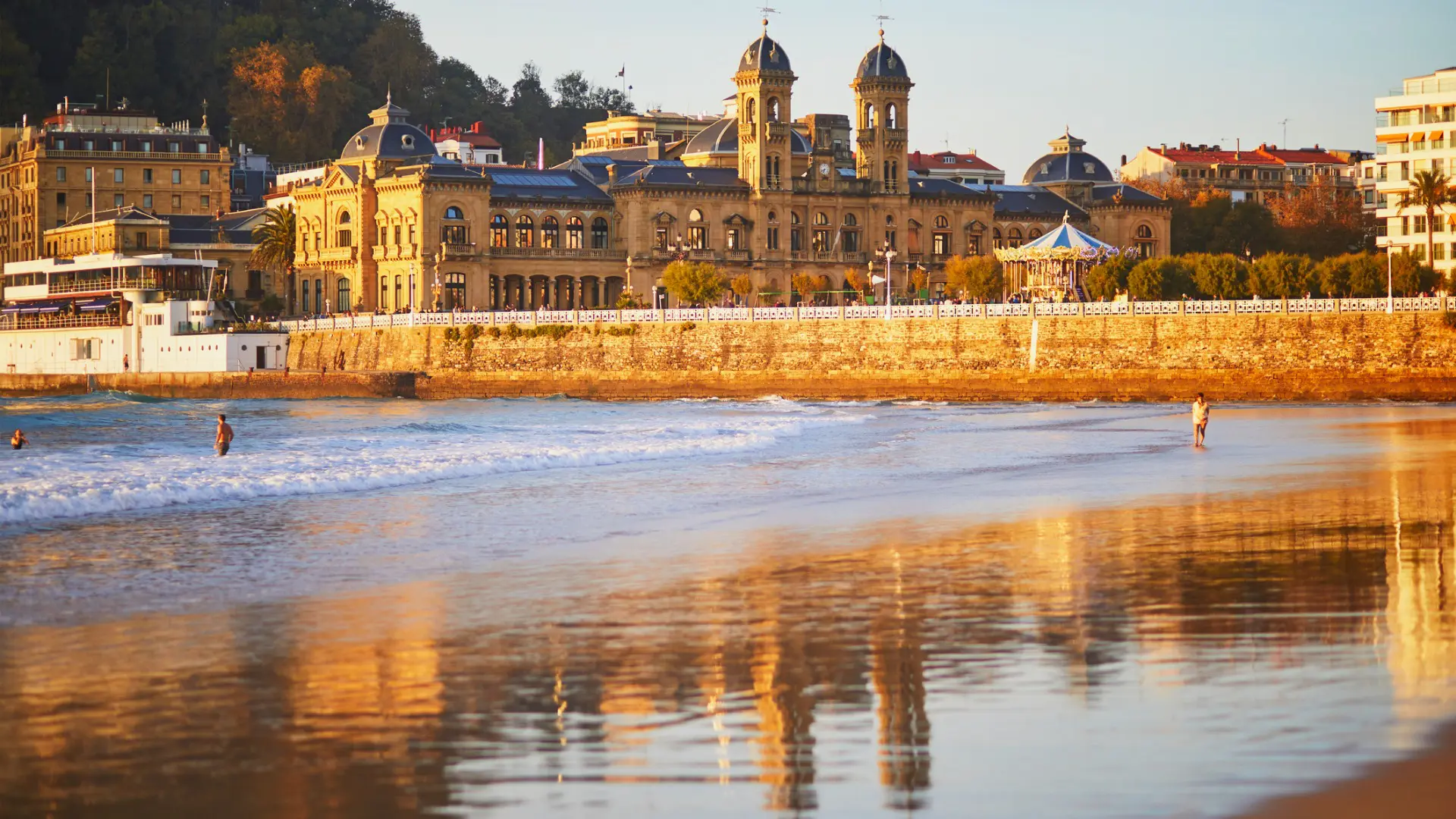 La Concha Beach in the foreground with grand buildings in the background, all dyed in golden sunlight.