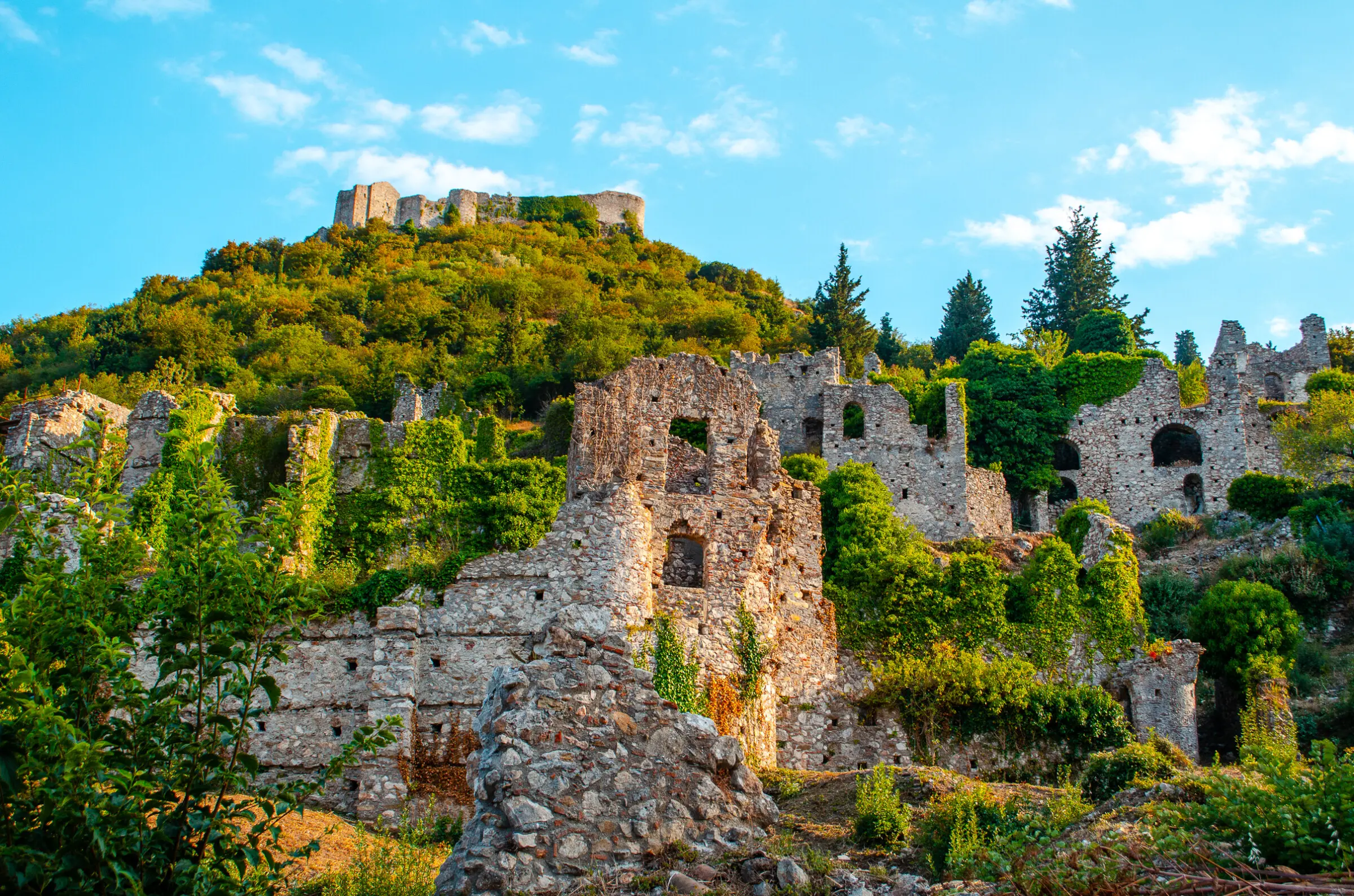 This image shows the medieval ruins of the castle town of Mystras amidst lush greenery.