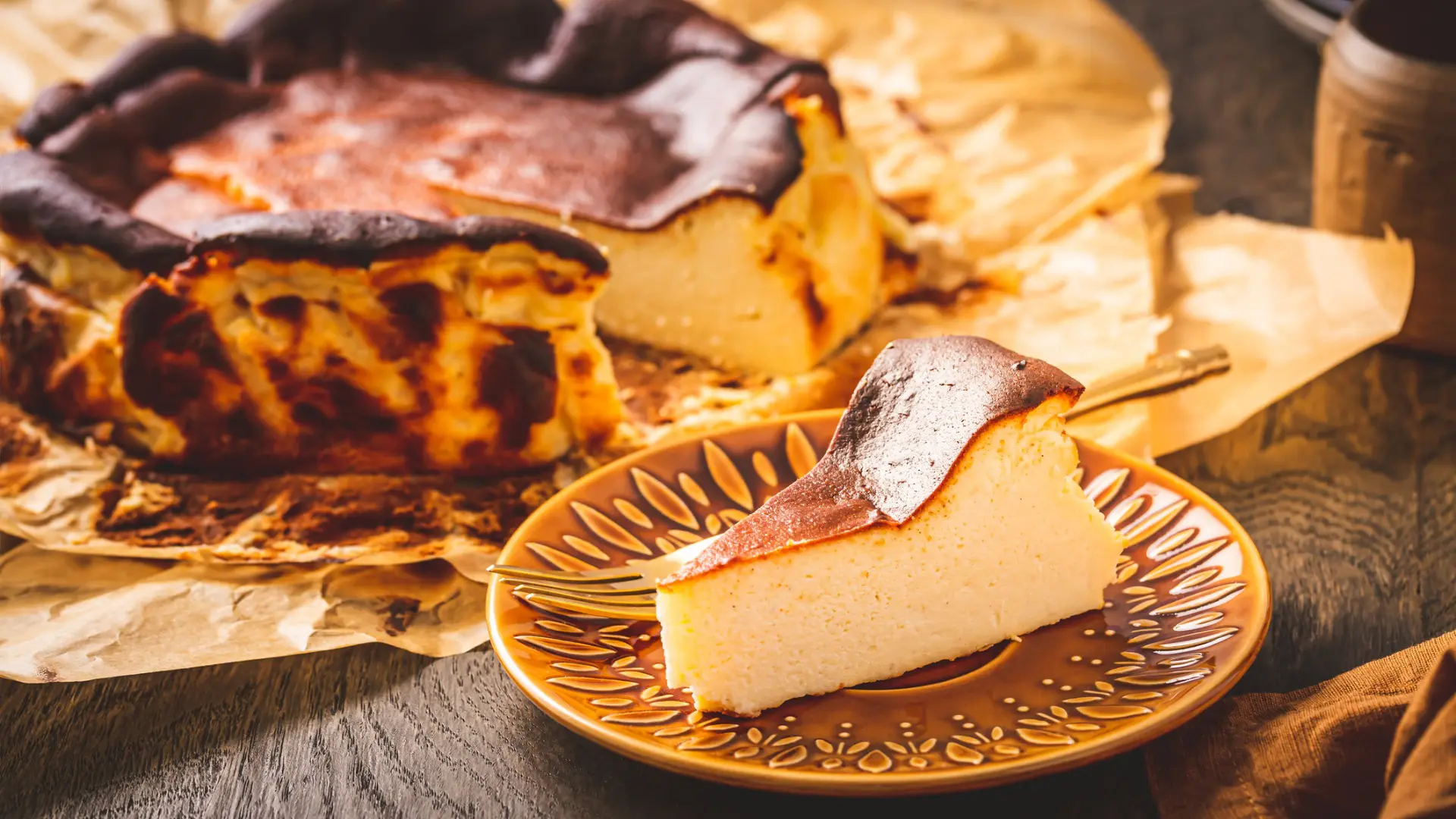 This image shows a piece of burnt cheesecake in the foreground with the rest of the cheesecake in the background.