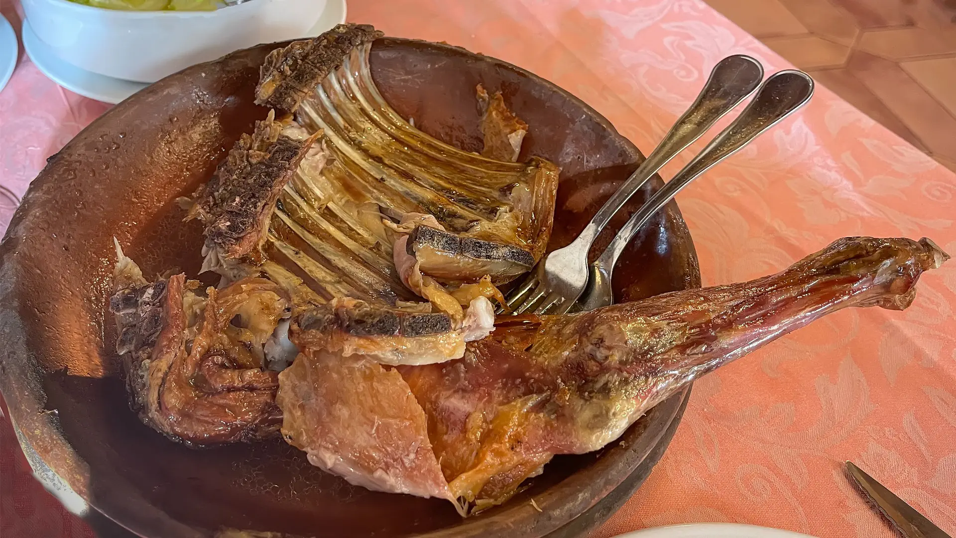 This image shows a piece of roasted suckling lamb in a clay dish.