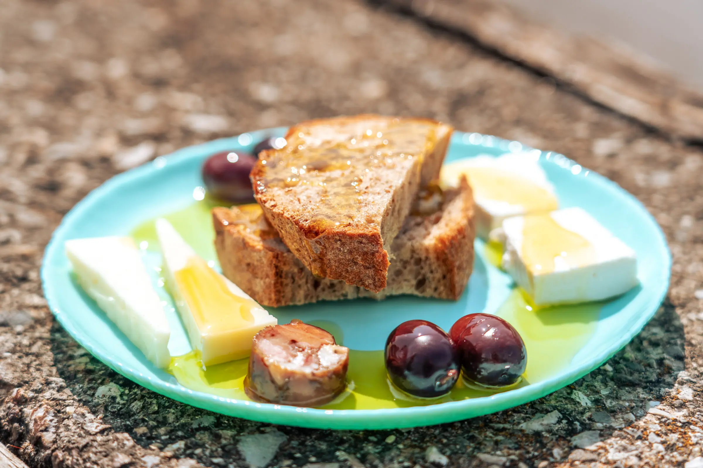A plate with pieces of bread, cheese, olives, all topped with olive oil.