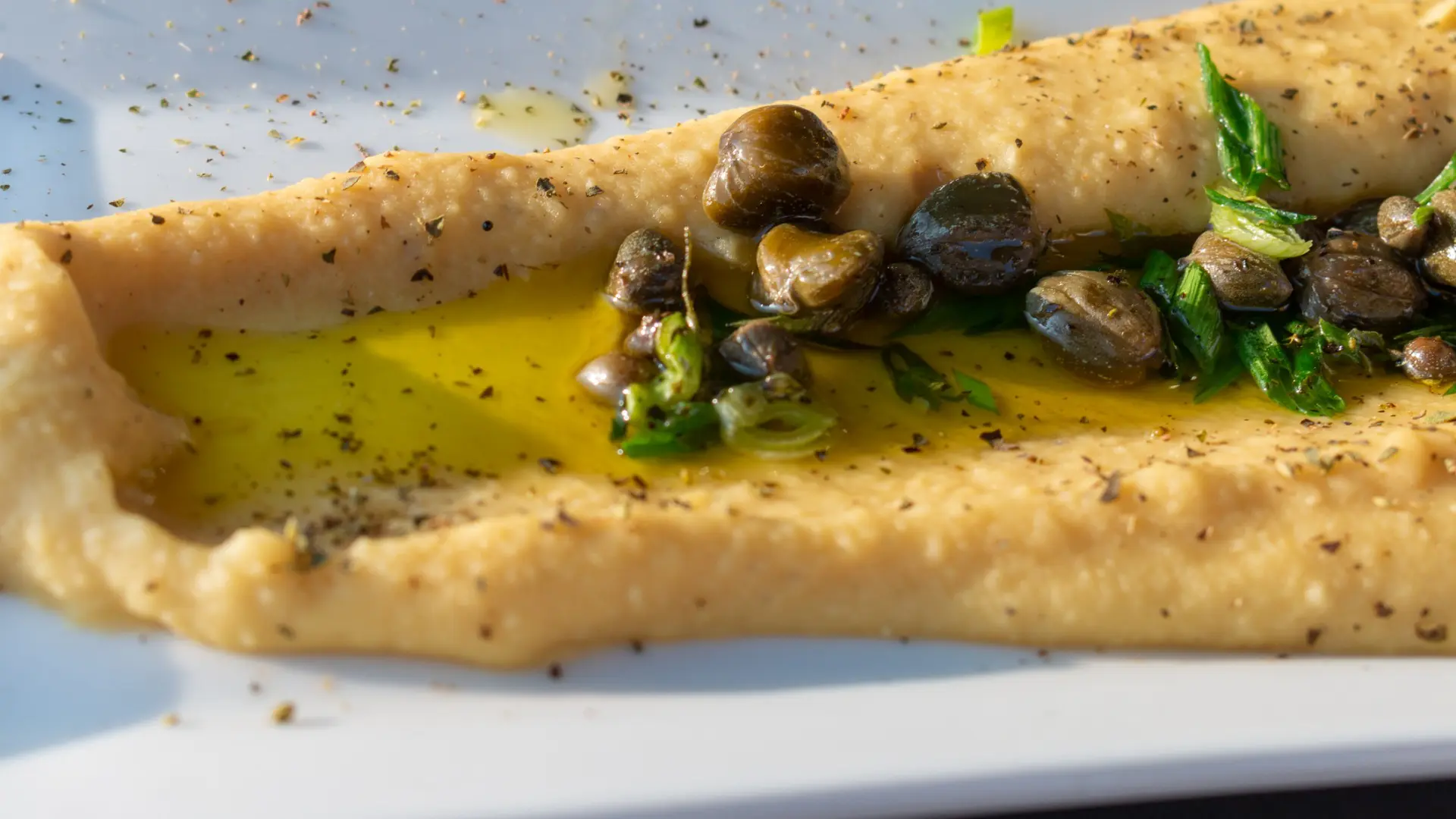 A close up of Fava puree topped with olive oil and capers.