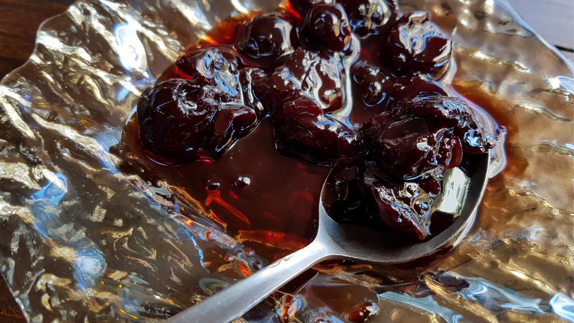 A close up of a spoon on a small glass plate filled with sour cherry spoon sweet.