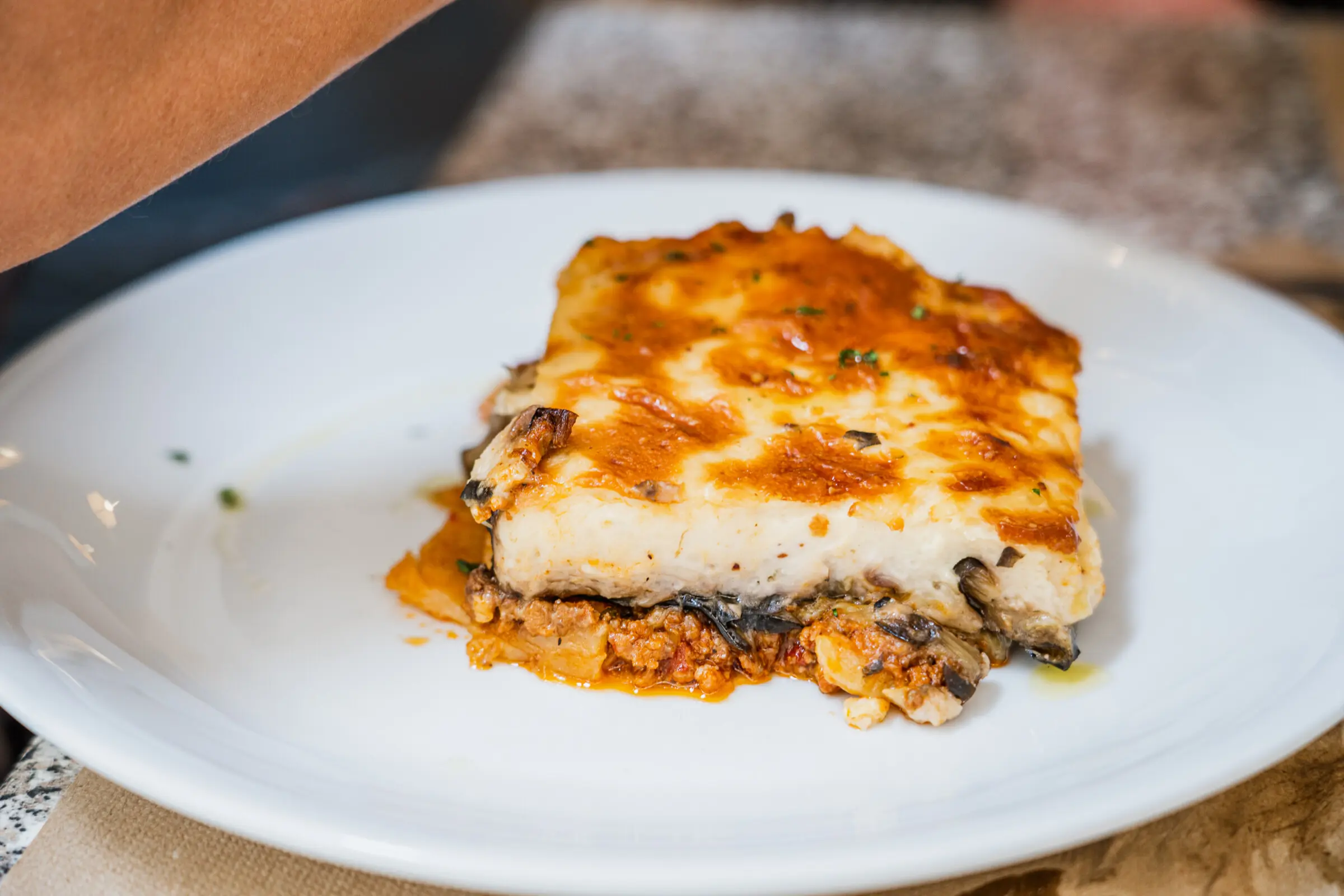 A close up of a white plate with a piece of Moussaka on it.
