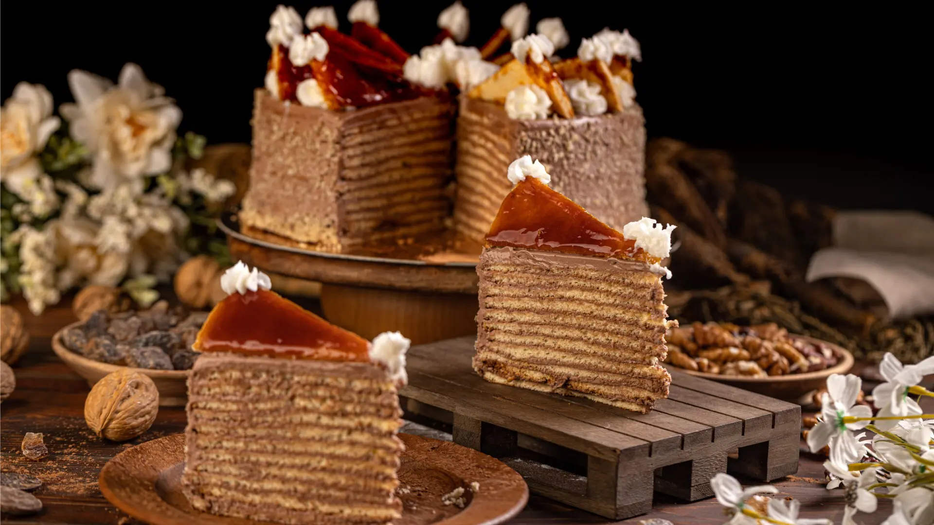 Two slices of Dobostorte with the rest of the cake in the background.