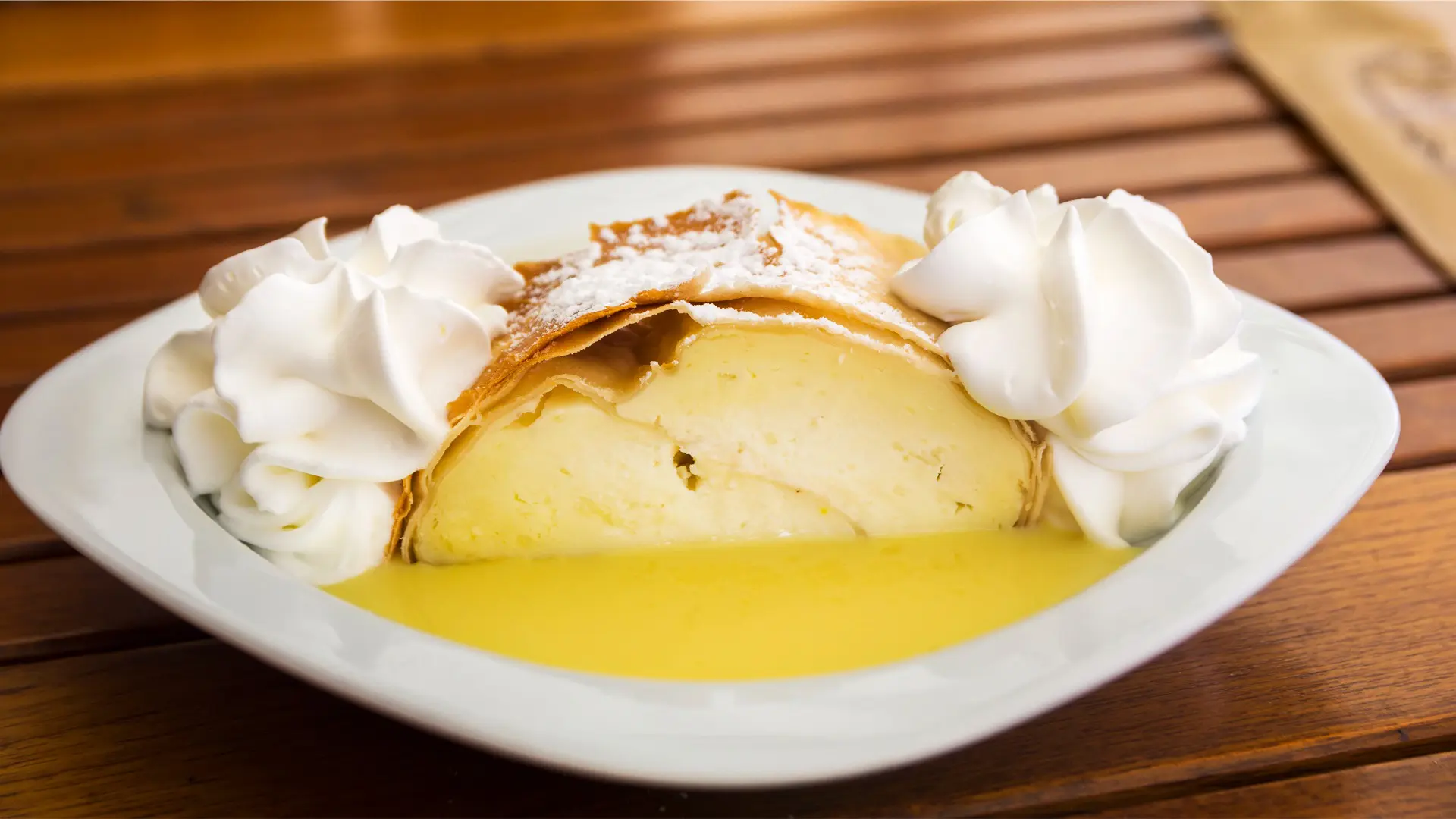 A close-up of Topfenstrudel with whipped cream and vanilla sauce on a wooden table.