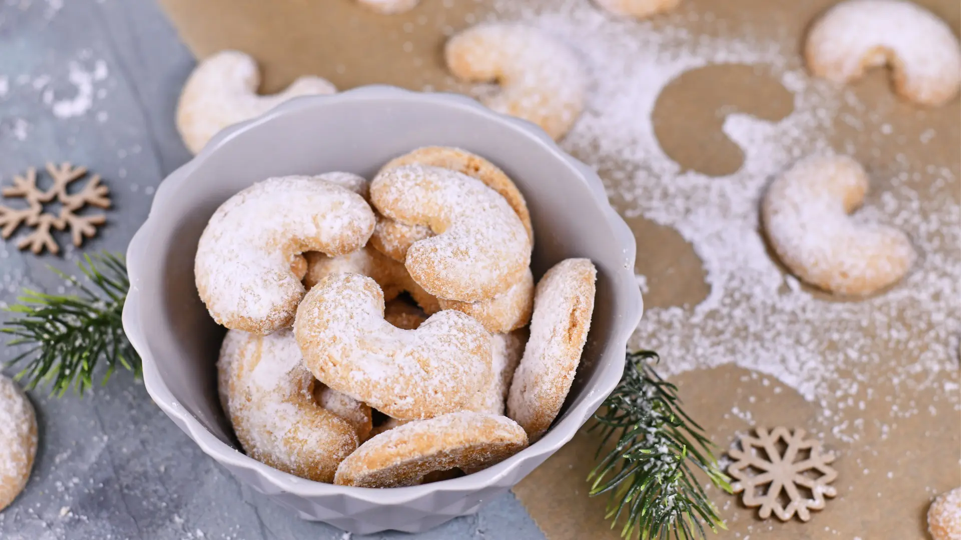 A bowl of crescent-shaped cookies sprinkled with icing sugar.