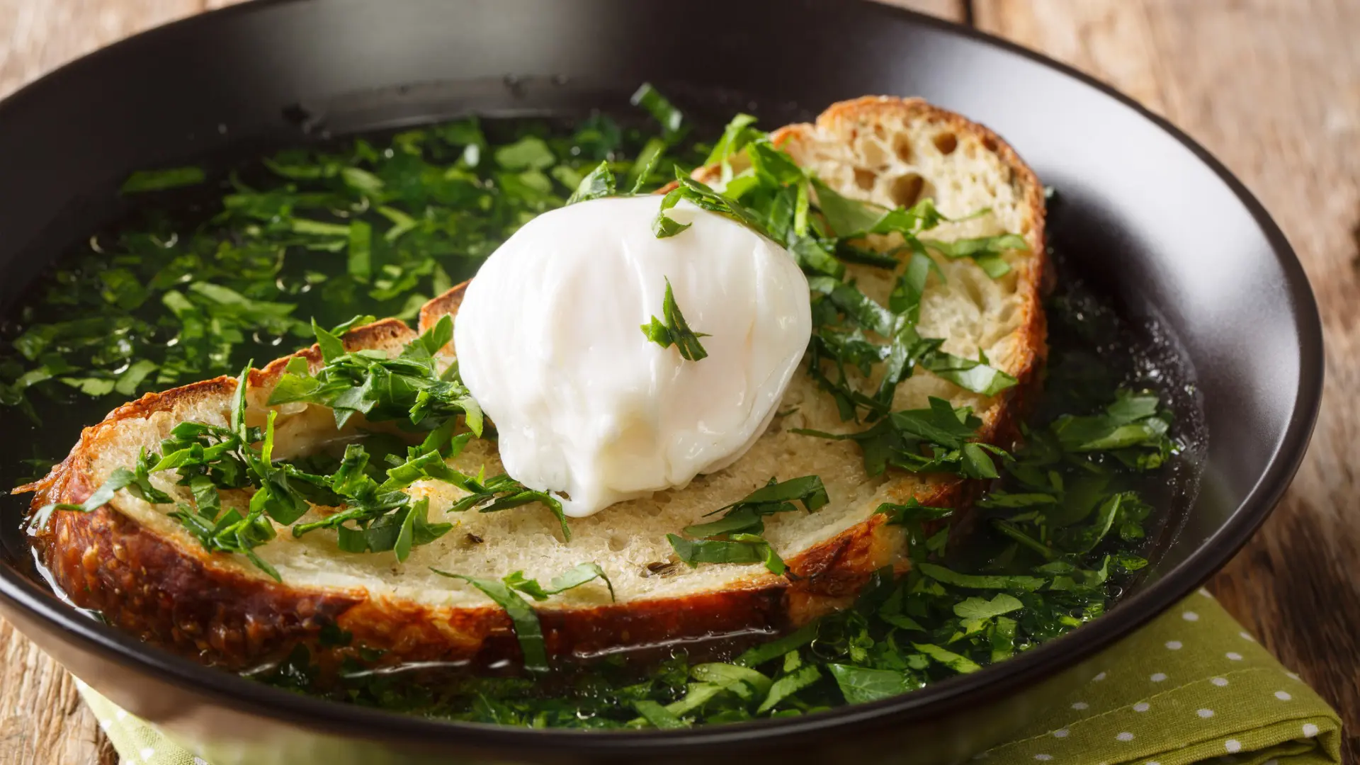 A close-up of a bowl filled with Acorda soup. It's full of greens and there's a slice of bread with a poached egg on top.