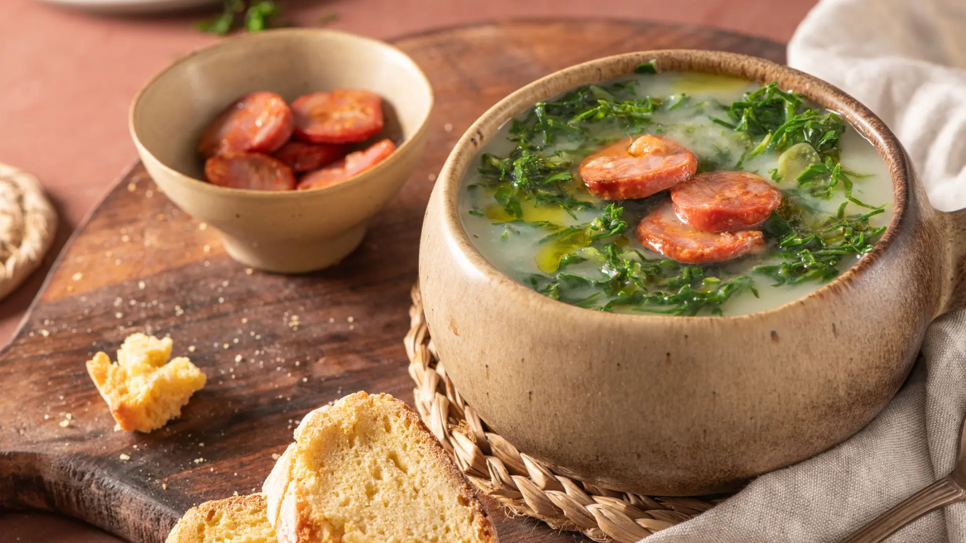 A close up of a bowl of Caldo Verde. Next to it, there's a smaller bowl with sausage slices.