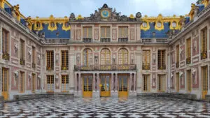 A detailed view of the ornate façade of the Palace of Versailles in France, showcasing its grand Baroque architecture. The building features elaborate decorations, including gold accents, sculpted reliefs, and large windows with yellow frames. The foreground highlights the striking black and white geometric patterned courtyard, which reflects the opulence and meticulous design of this historic royal residence. The scene captures the splendor and elegance of one of Europe's most famous palaces.