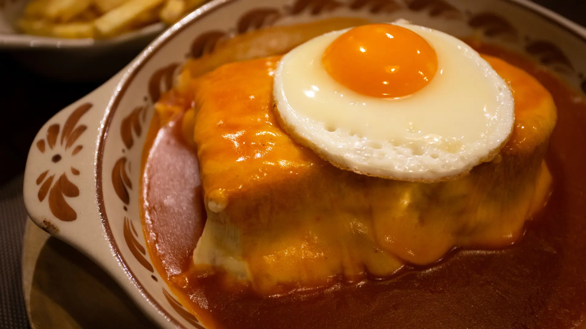 A close up of a Francesinha sandwich doused in a red sauce and topped with a fried egg.