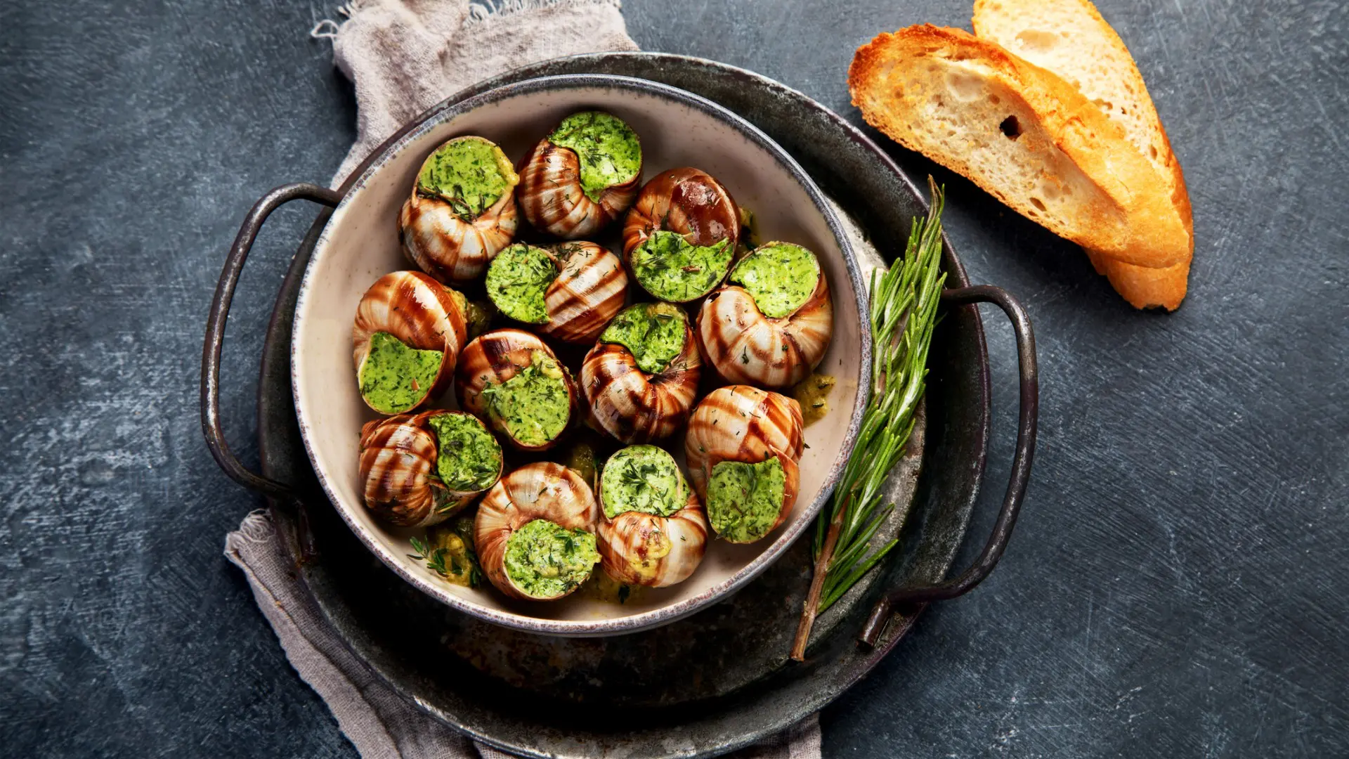 Snails with herbs and butter served with two slices of baguette bread.