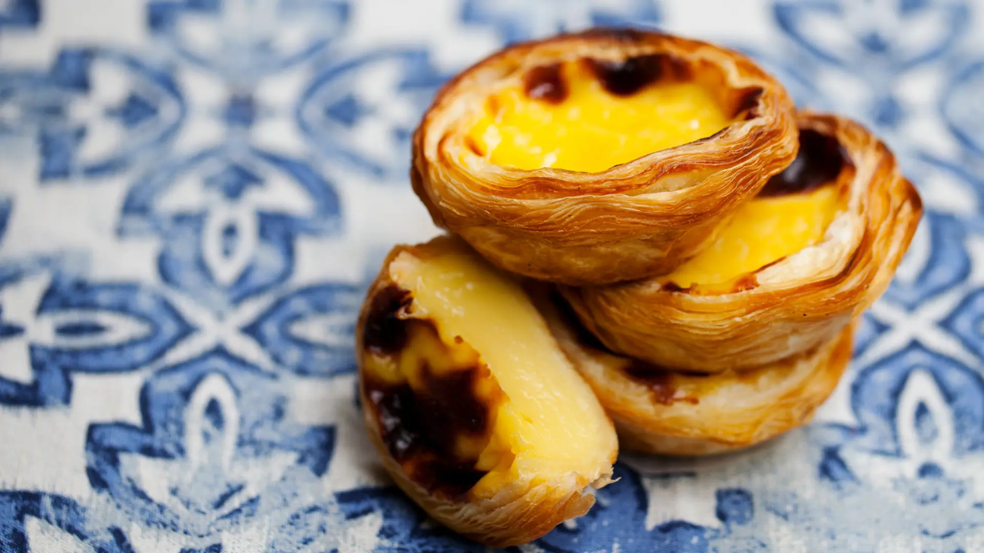 A close up of four Pasteis de Nata against a blue and white-tile background.