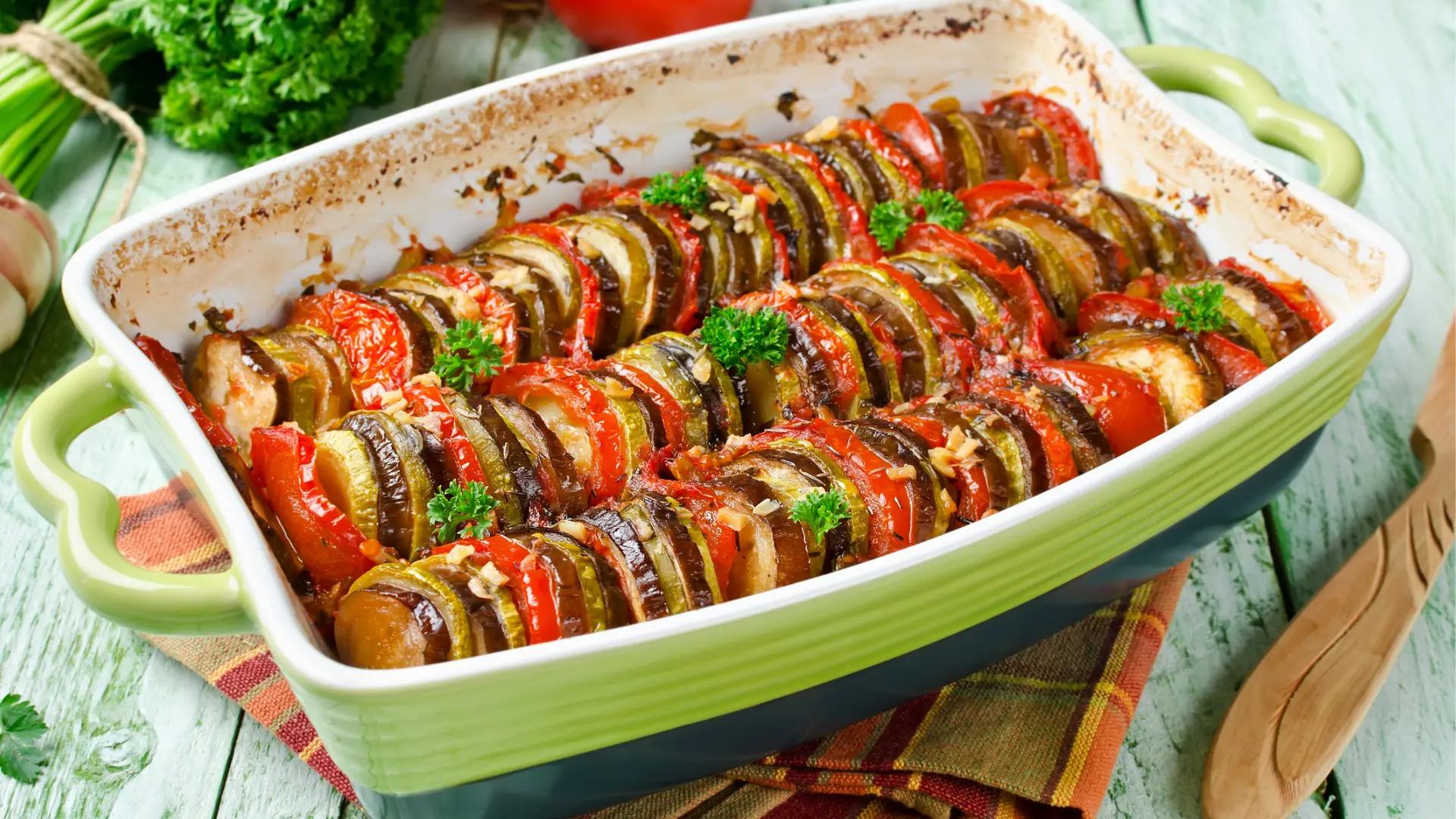 A light-green ceramic baking dish with rows of vegetables: green bell peppers, eggplant, and zucchini.