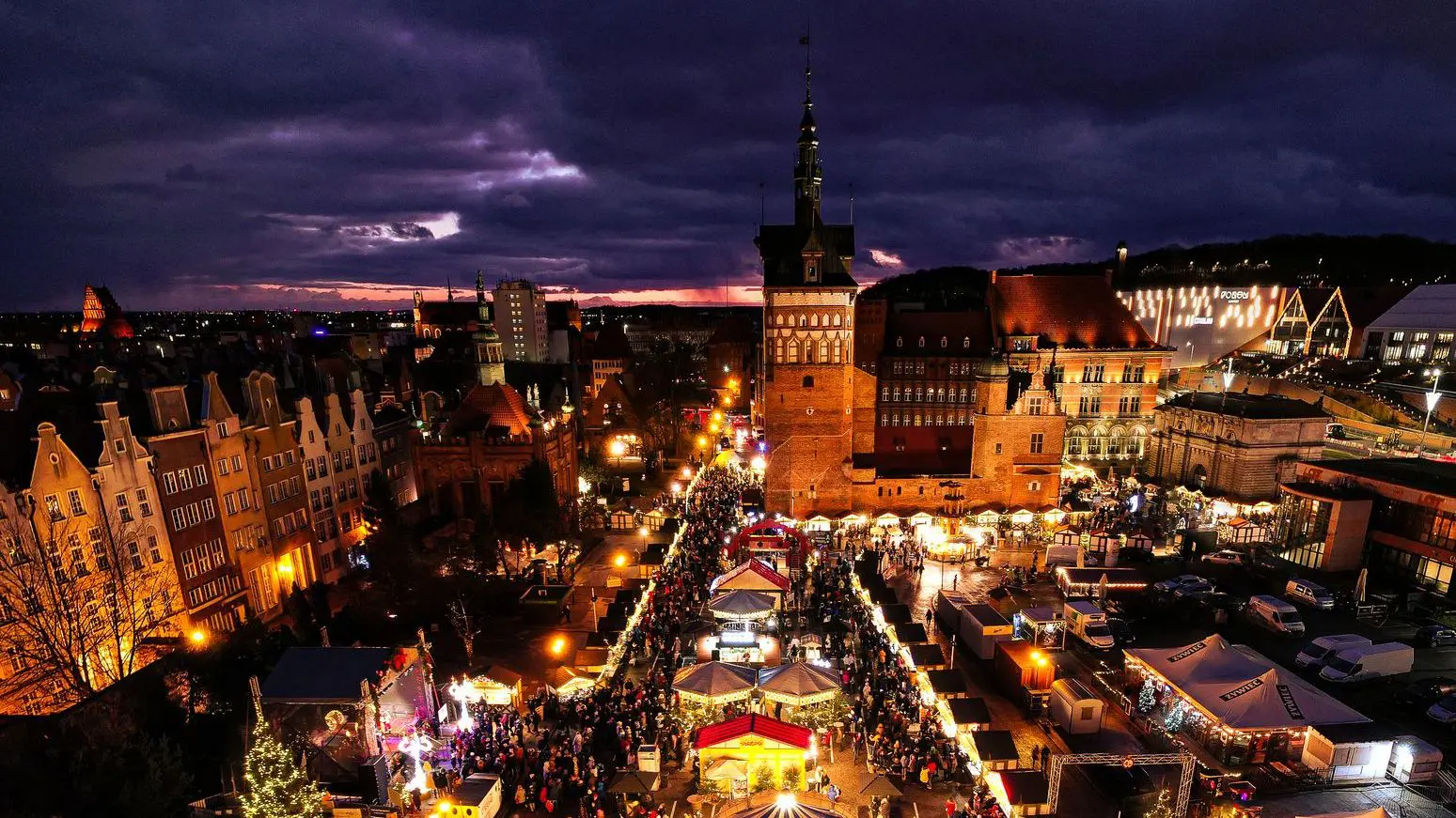 An aerial view of Gdansk's Christmas market under a dramatic sky. There are crowds of people.