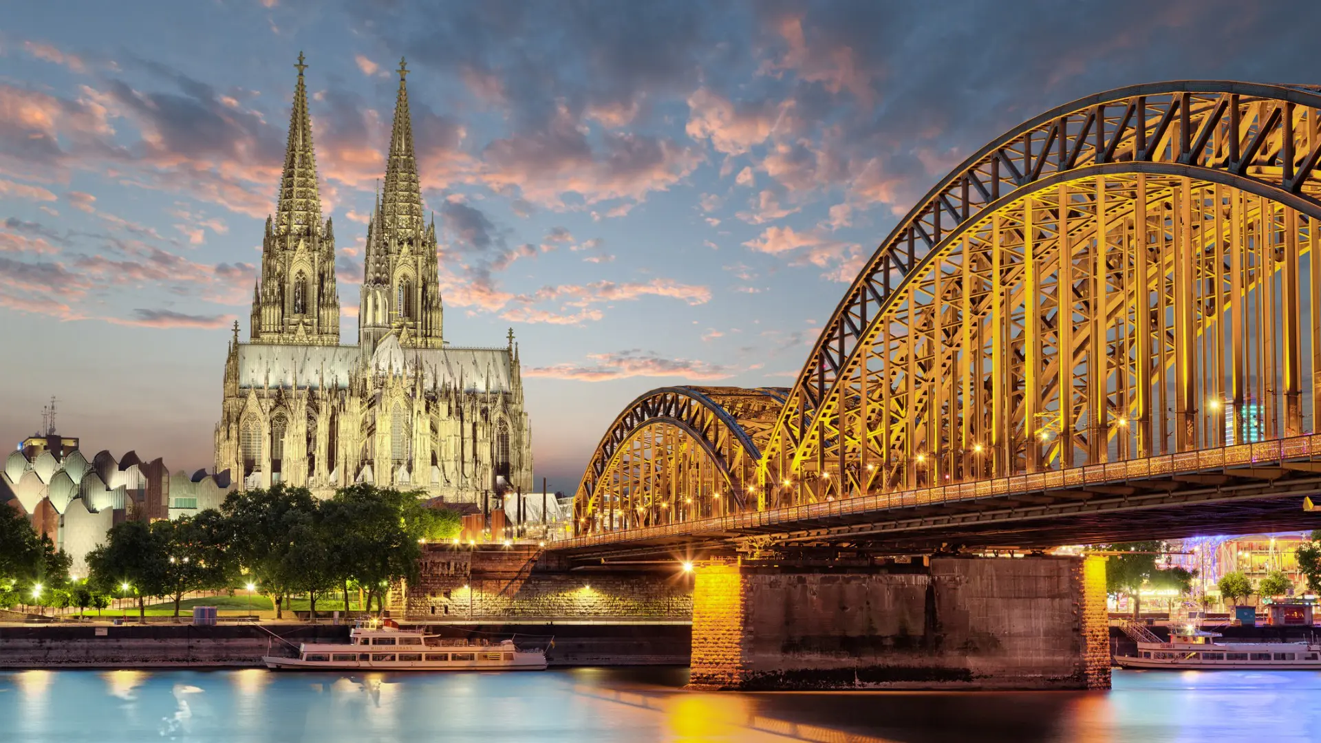 An imposing Cathedral under a blue sky with pink clouds, next to an impressive bridge.