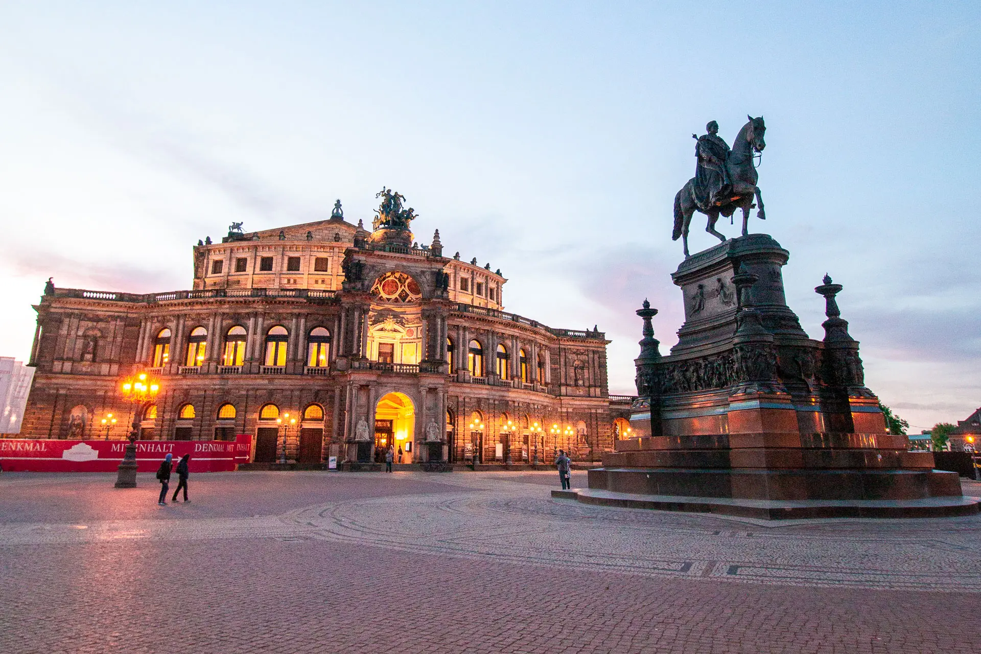 A beautifully lit building and a large statue of a man riding a horse on a quiet square.