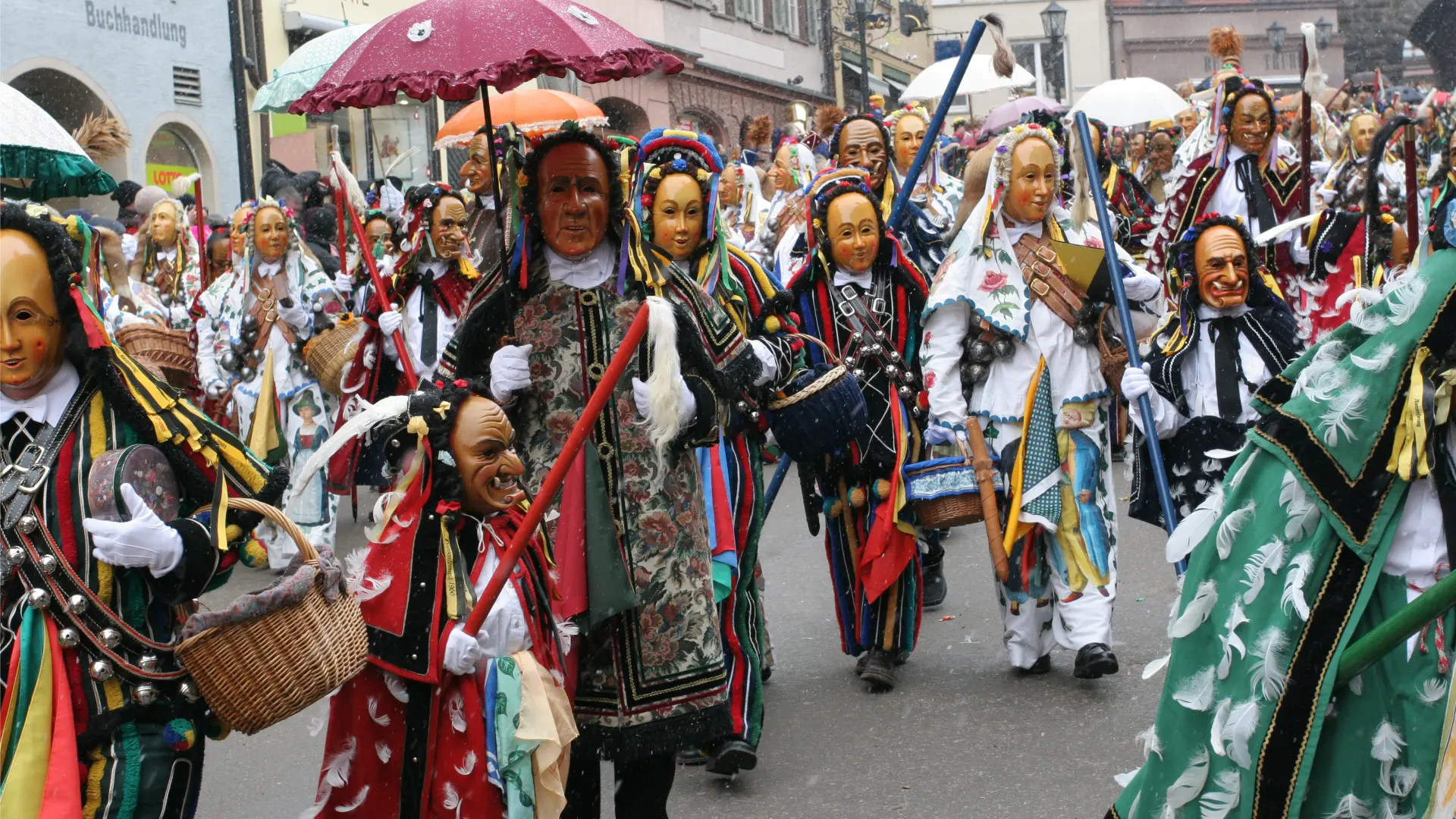 Several people with masks and costumes parading along a street.