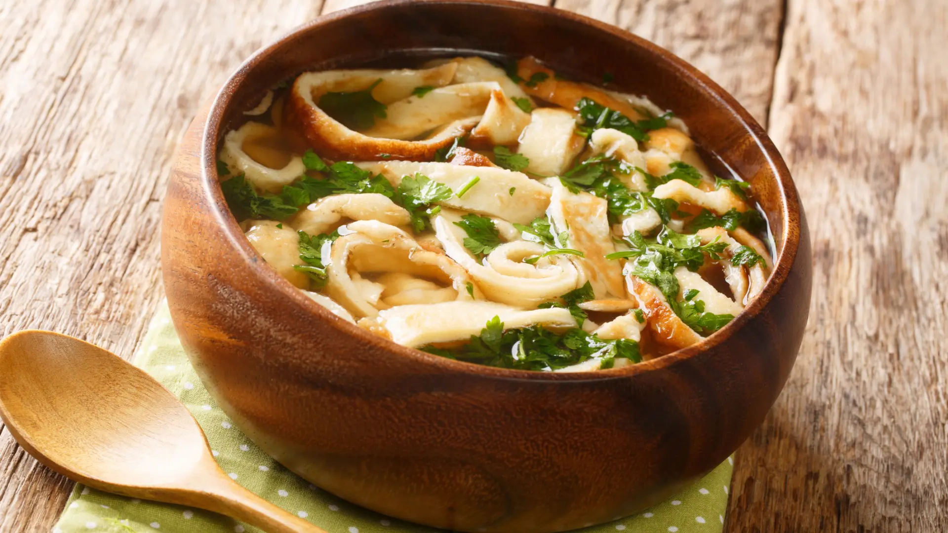 A wooden bowl filled with soup made of pancake strips and greens. Frittatensuppe is the best Austrian food for comfort.
