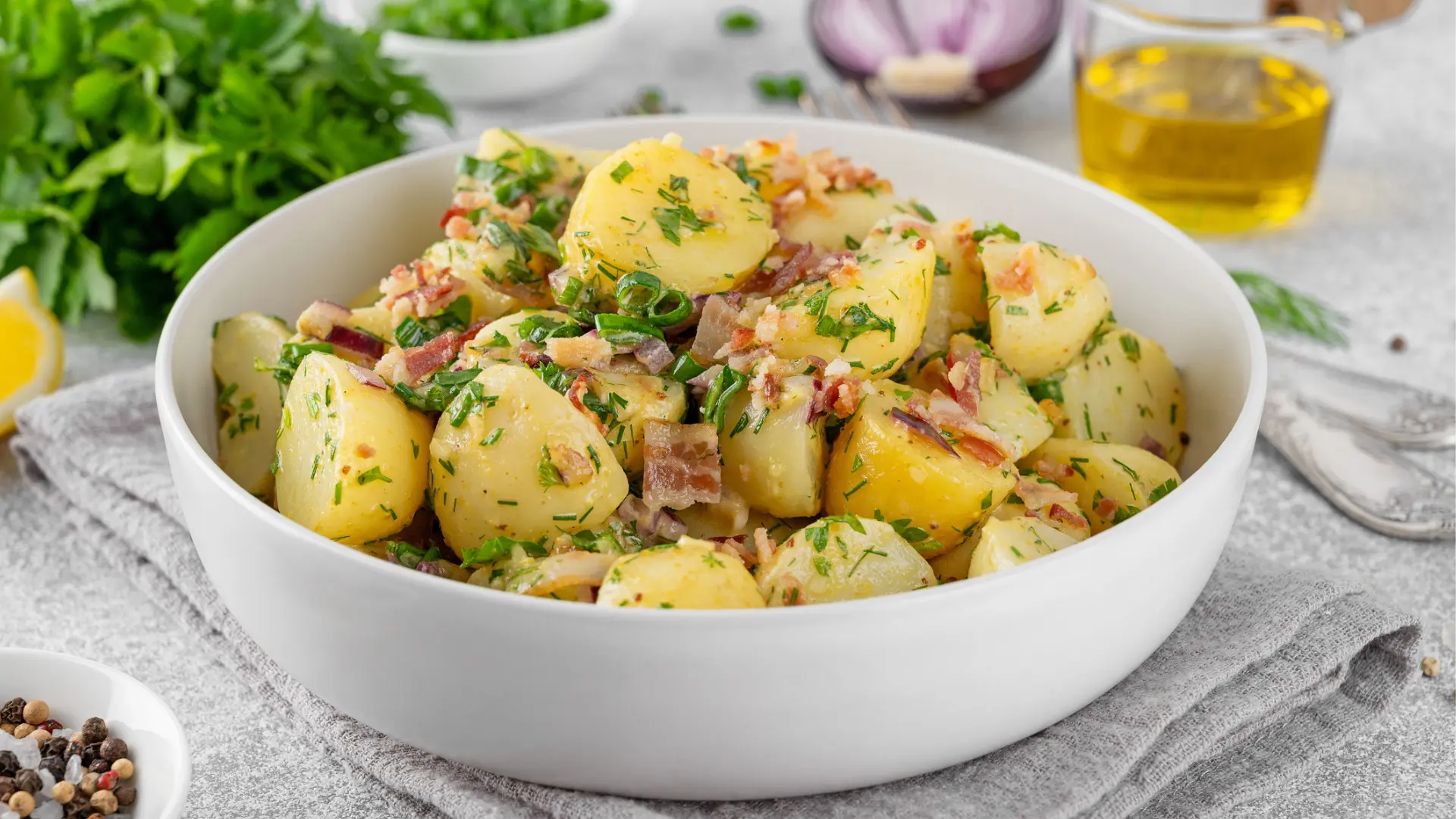 A white bowl with boiled potatoes, small bacon pieces and greens.