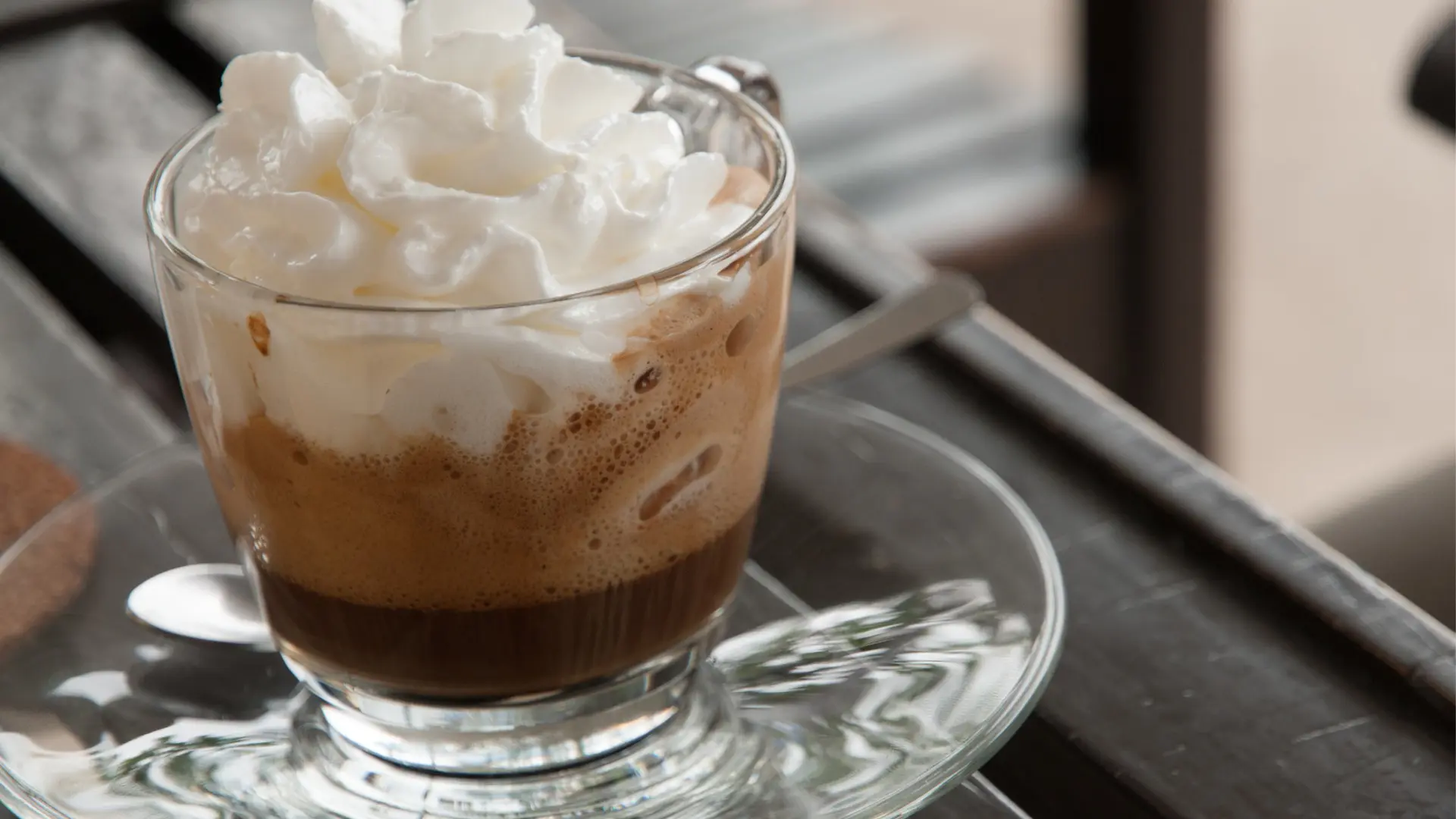 A close up of a glass espresso cup topped with whipped cream.