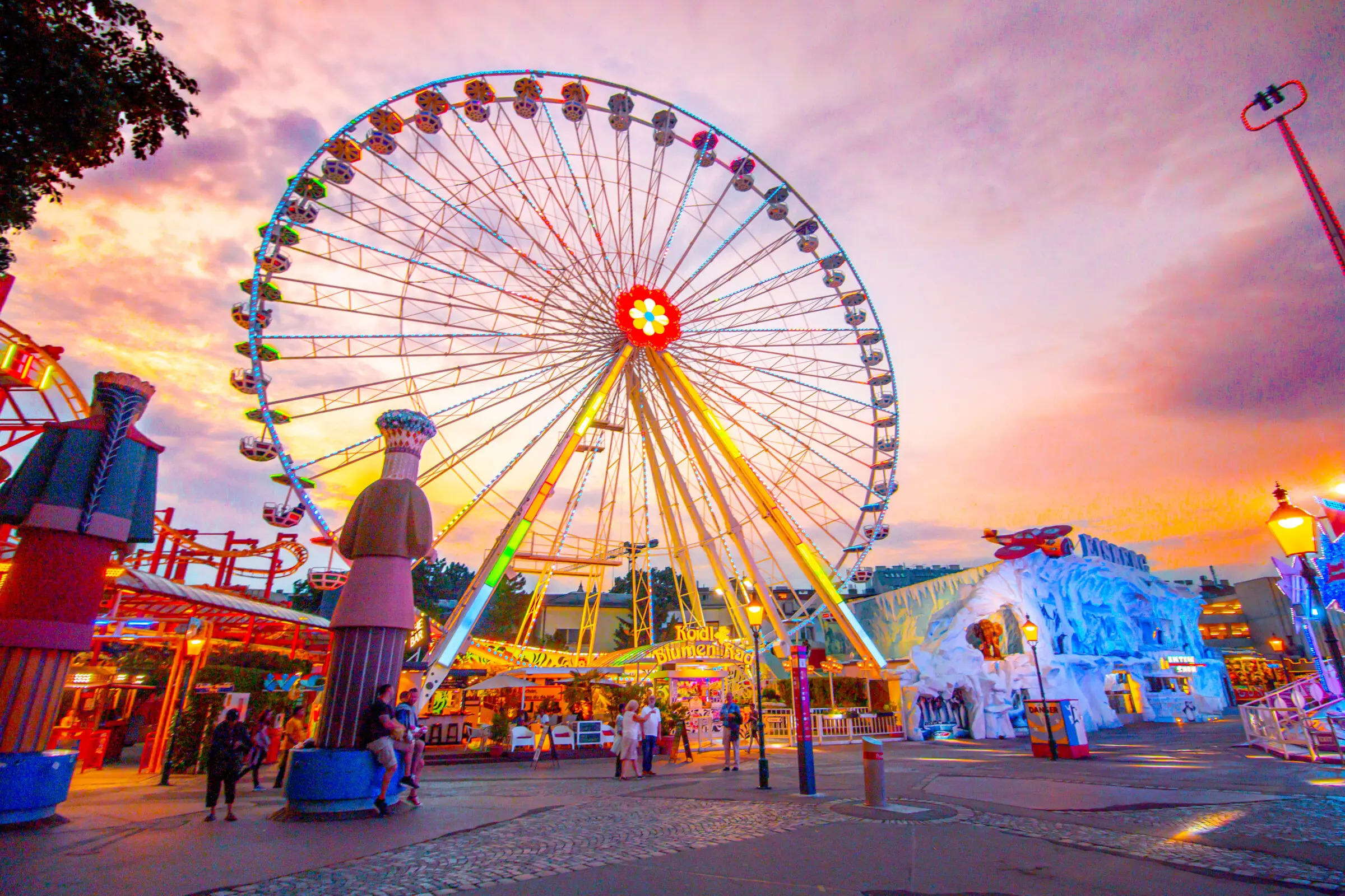 A Ferris Wheel at an amusement park under a pink and orange sunset sky.