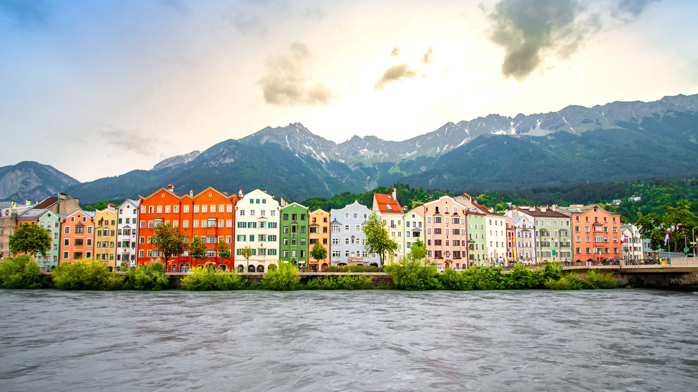 A row of colorful buildings by the water with tall mountains in the background. 