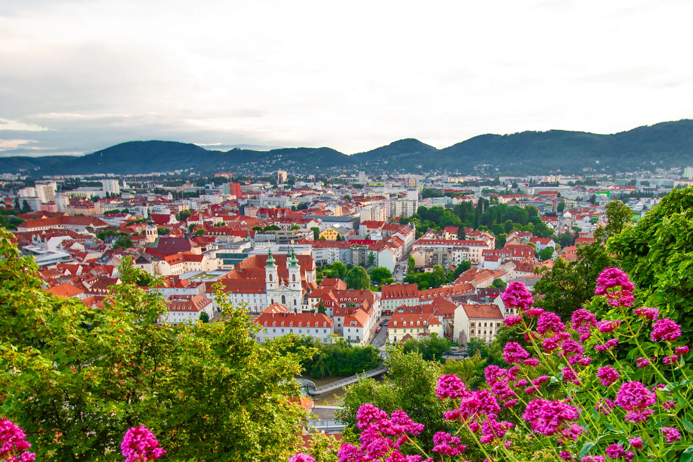 A panoramic view of Graz's red rooftops with flowers in the foreground. For many, spring is the best time to visit Austria. 