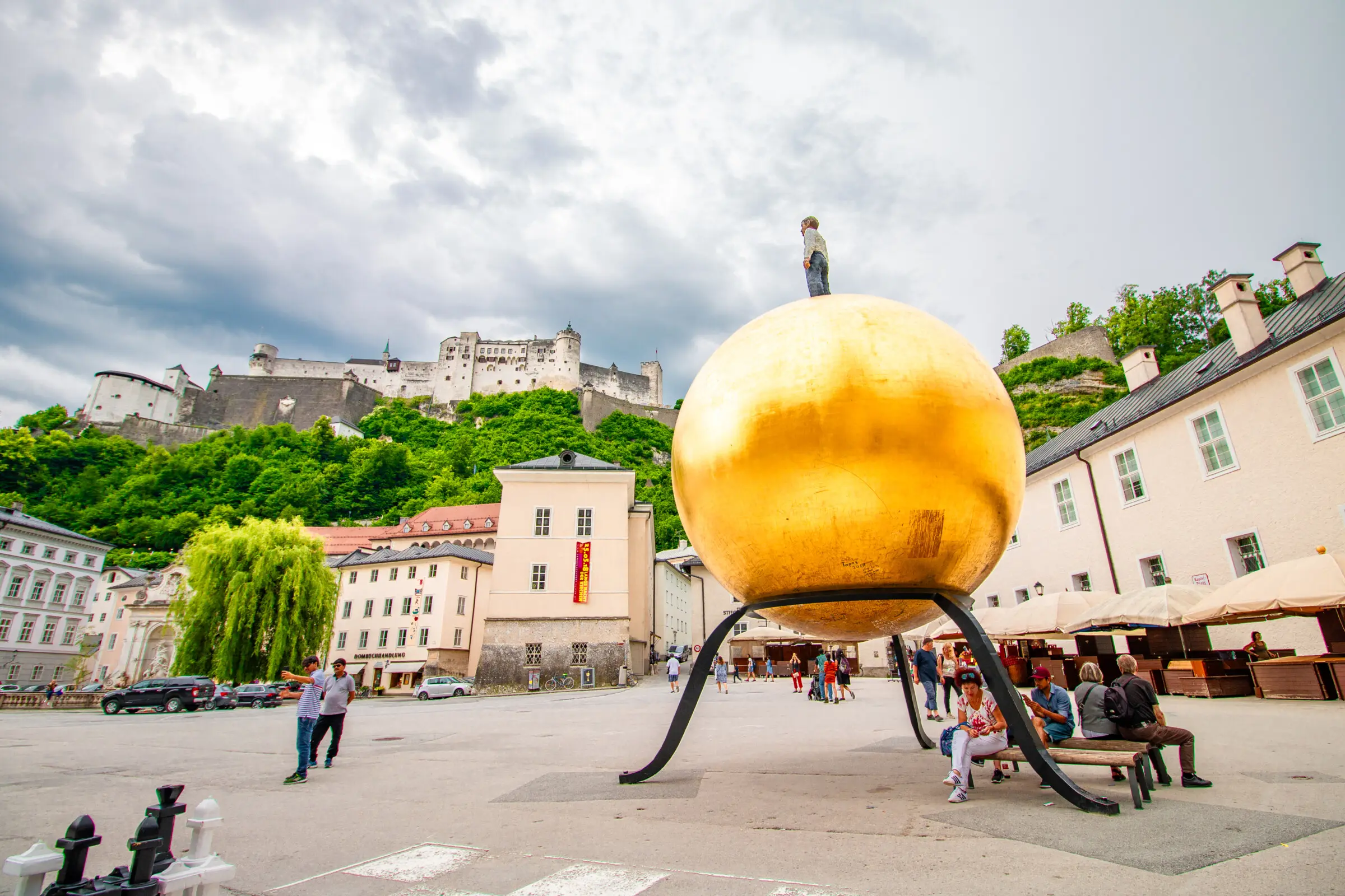A square in Salzburg dominated by a huge golden sphere. In the background, a hilltop castle. 