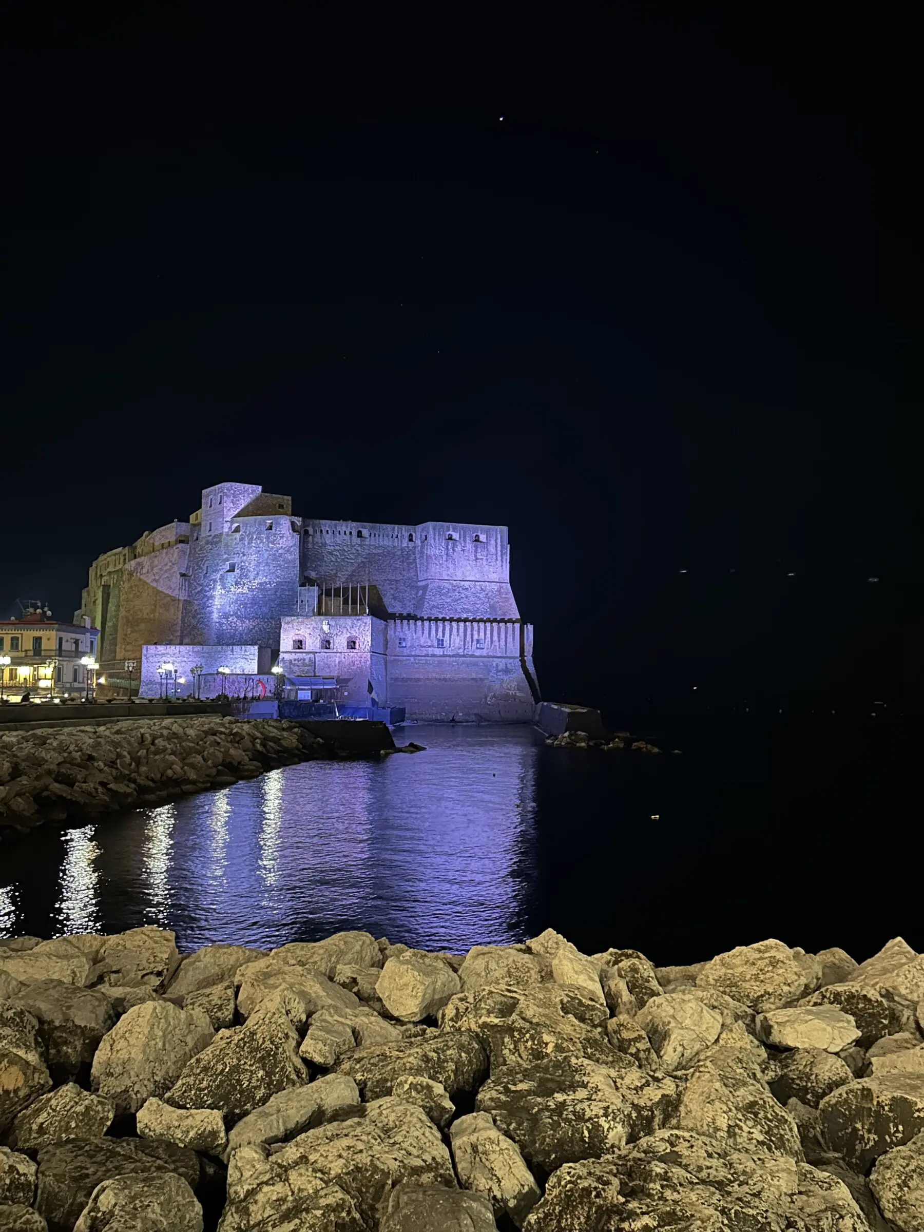 A night shot of Castel dell'Ovo with the sea in the foreground.