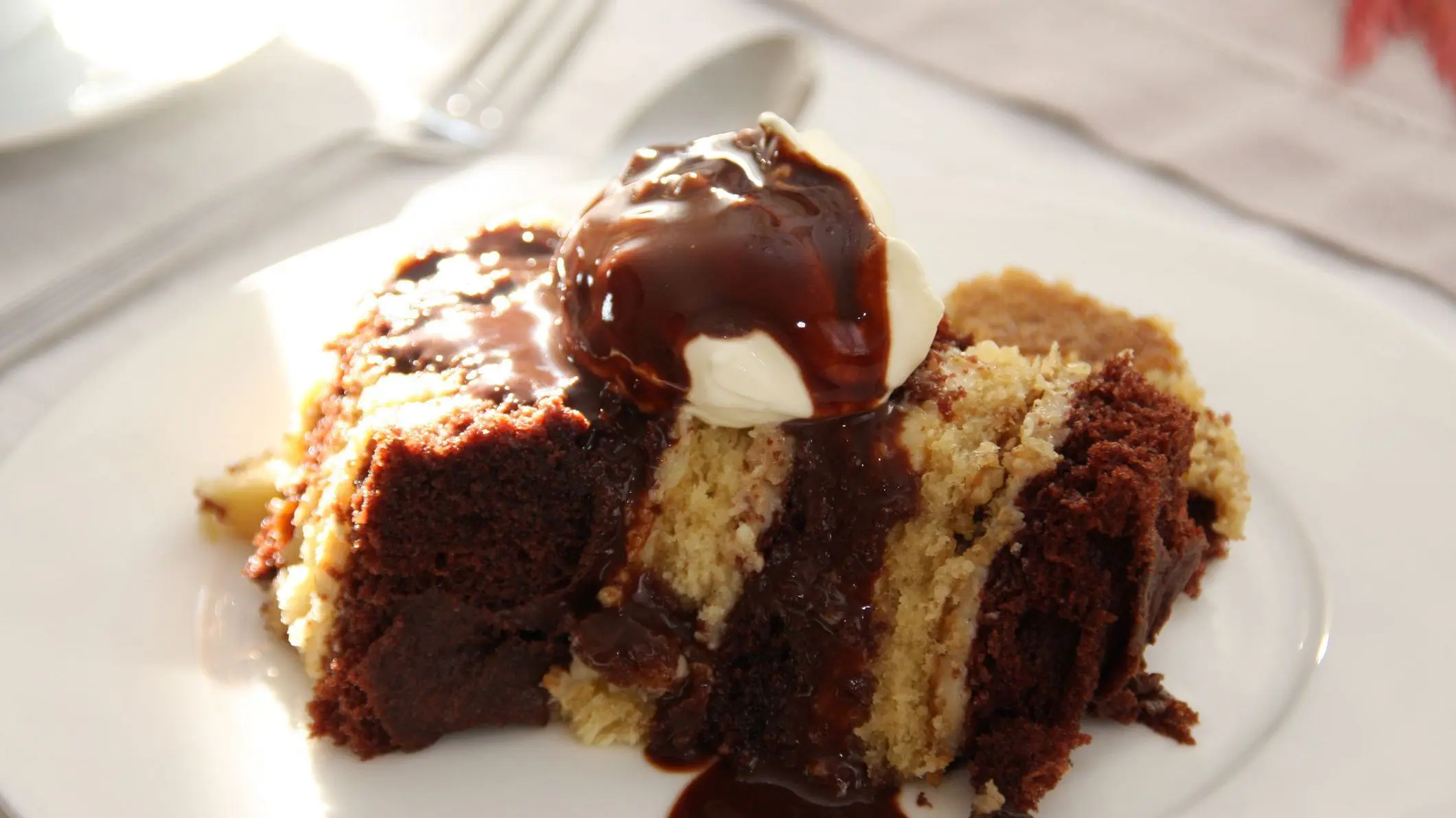 Layered cake served with chocolate sauce and whipped cream on a white plate. 