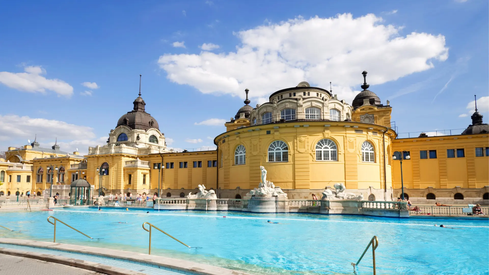 A beautiful yellow building with a large outdoor pool in the foreground.