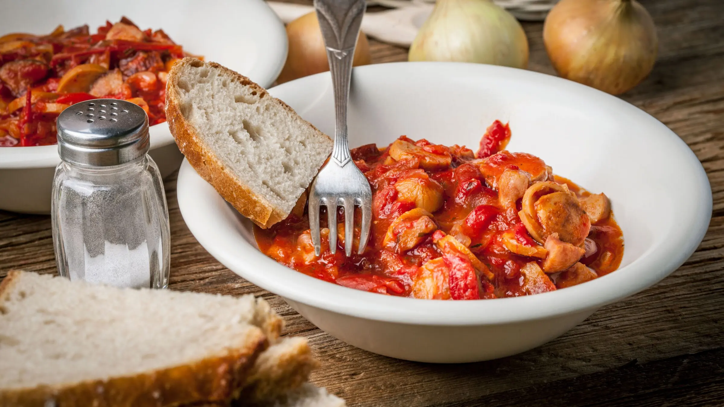 A white plate with a vegetable and sausage stew and a slice of bread on the side. 
