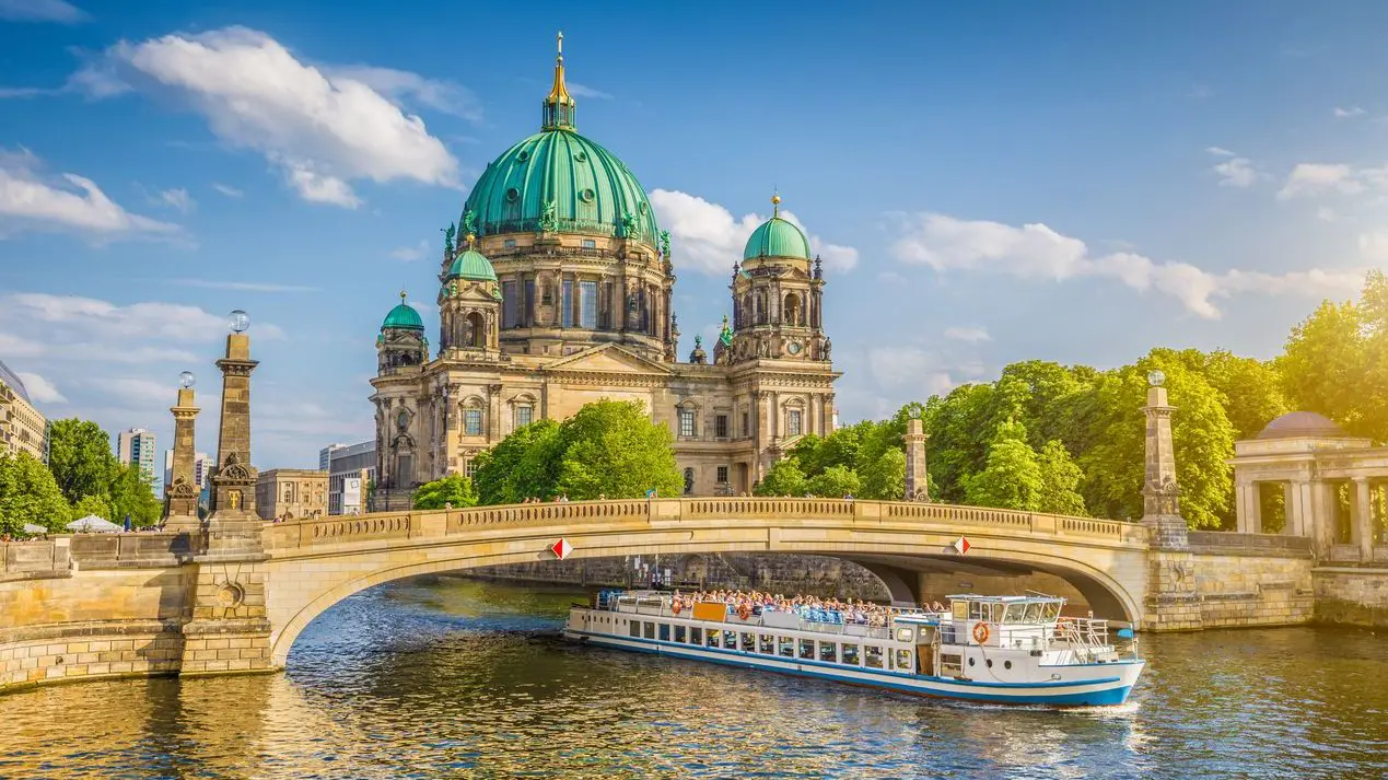 Beautiful view of the historic Berlin Cathedral on the famous Museum Island with a ship passing under Friedrichsbrucke Bridge on the Spree River in golden evening light at sunset in the summer.