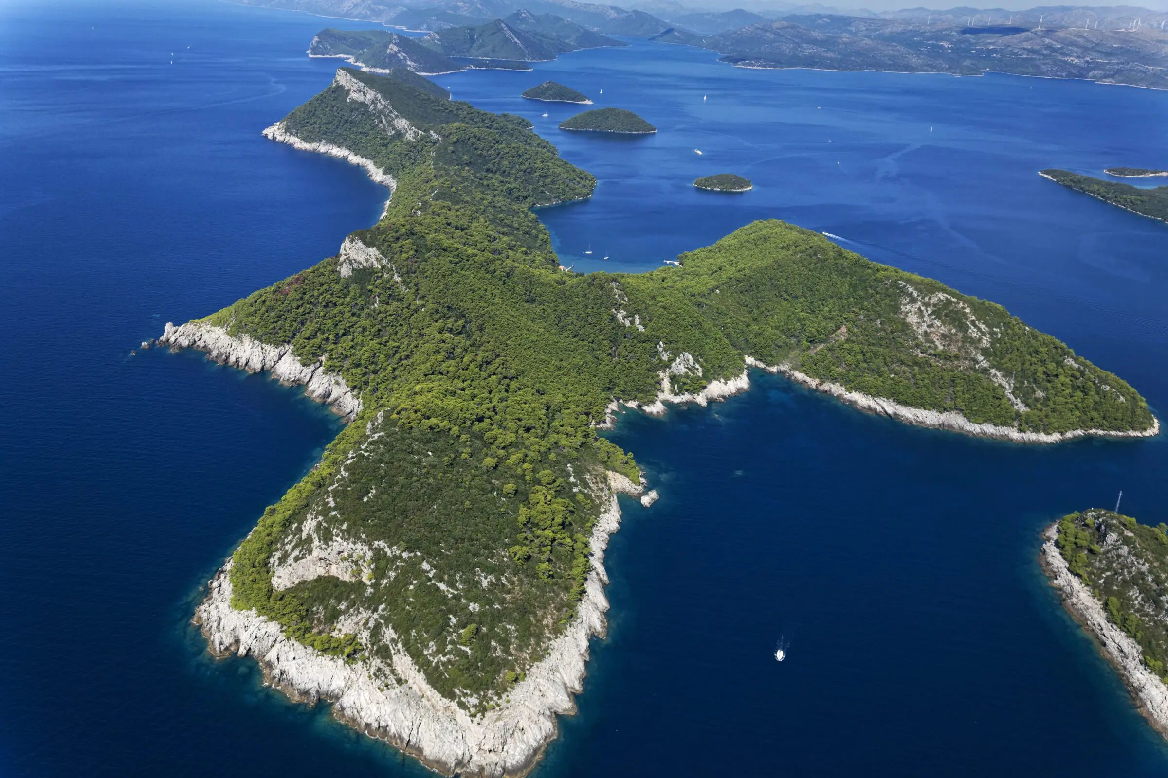 Aerial view of the Elafiti Islands off the coast of Dubrovnik, featuring rugged coastlines, lush green forests, and deep blue Adriatic waters dotted with sailboats.
